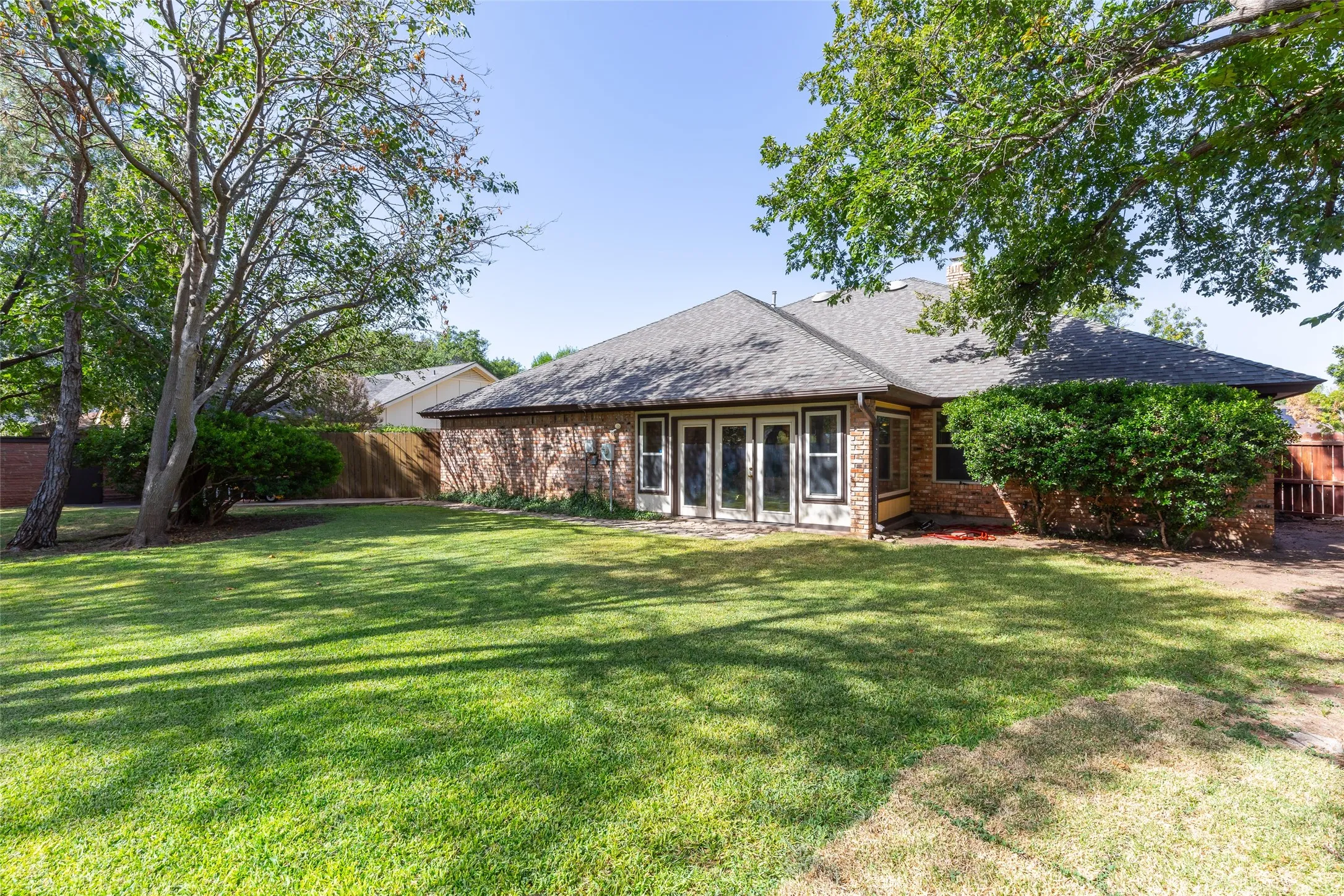 Expansive backyard featuring mature trees, a manicured lawn, and brick exterior