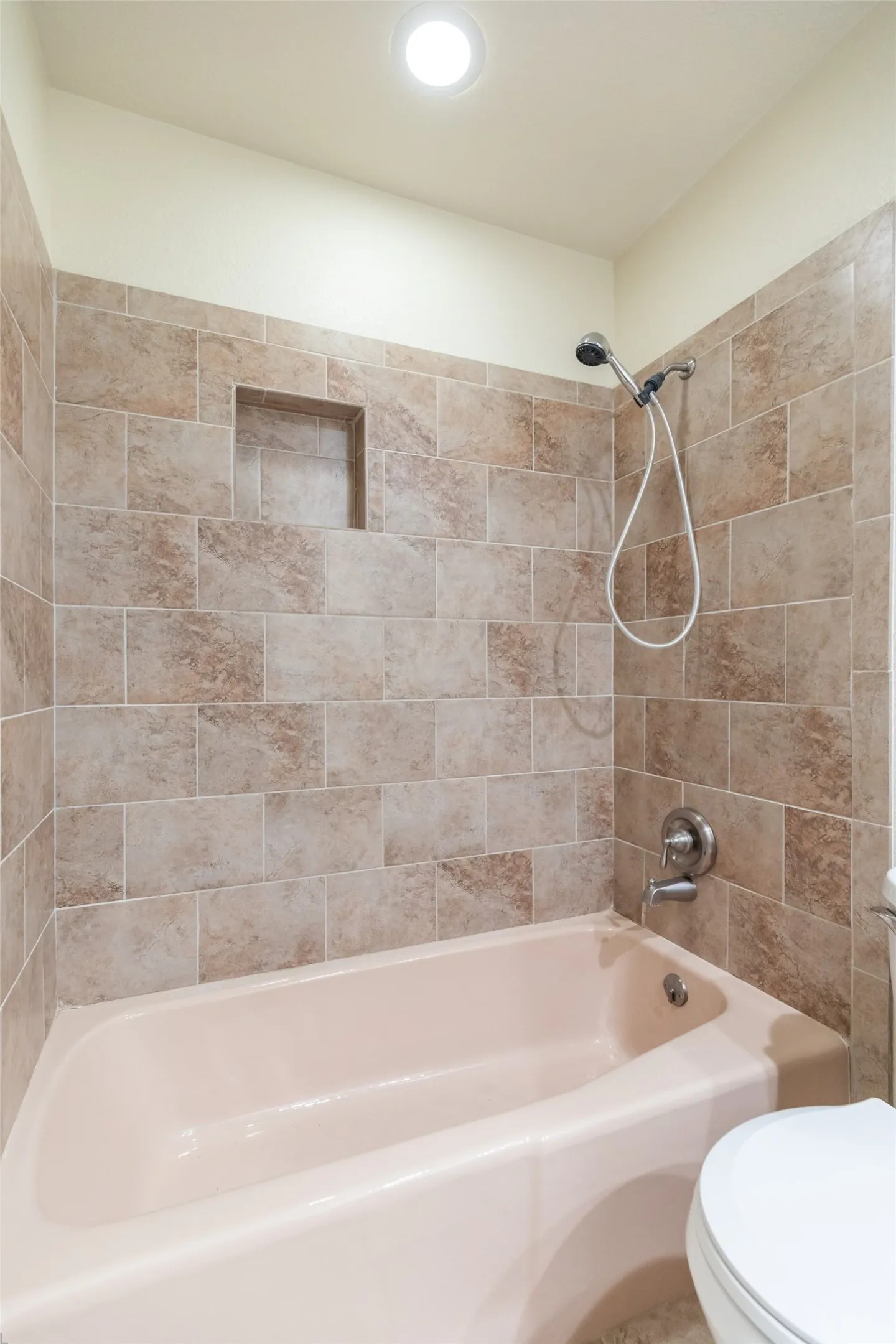 Tub and shower combination with tiled surround, recessed shower niche, and ceiling-mounted lighting