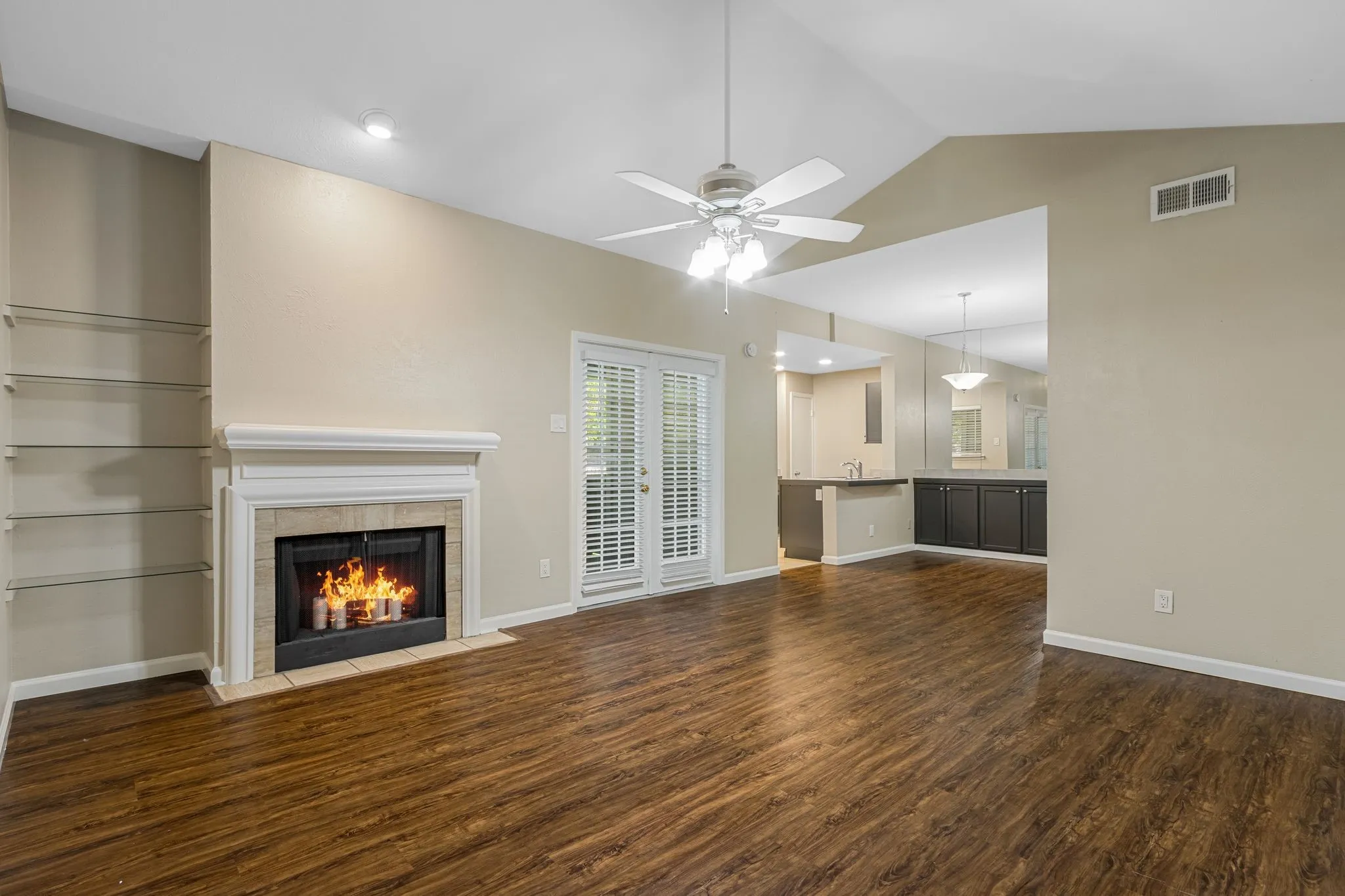 Unfurnished living room with dark wood-style floors, vaulted ceiling, a tile fireplace, and a ceiling fan