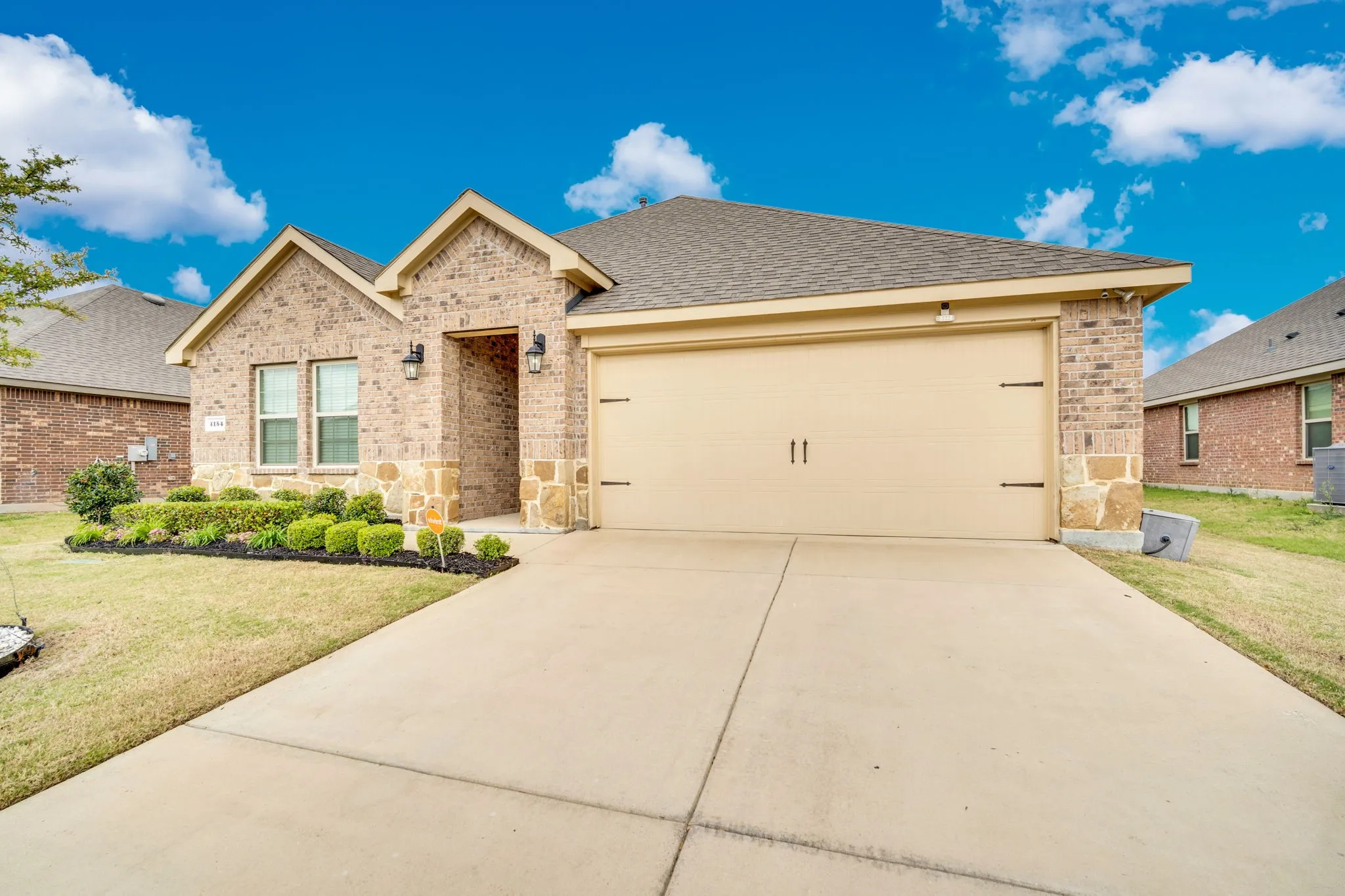 Brick and stone facade, attached garage, concrete driveway, landscaped front yard, and covered entry