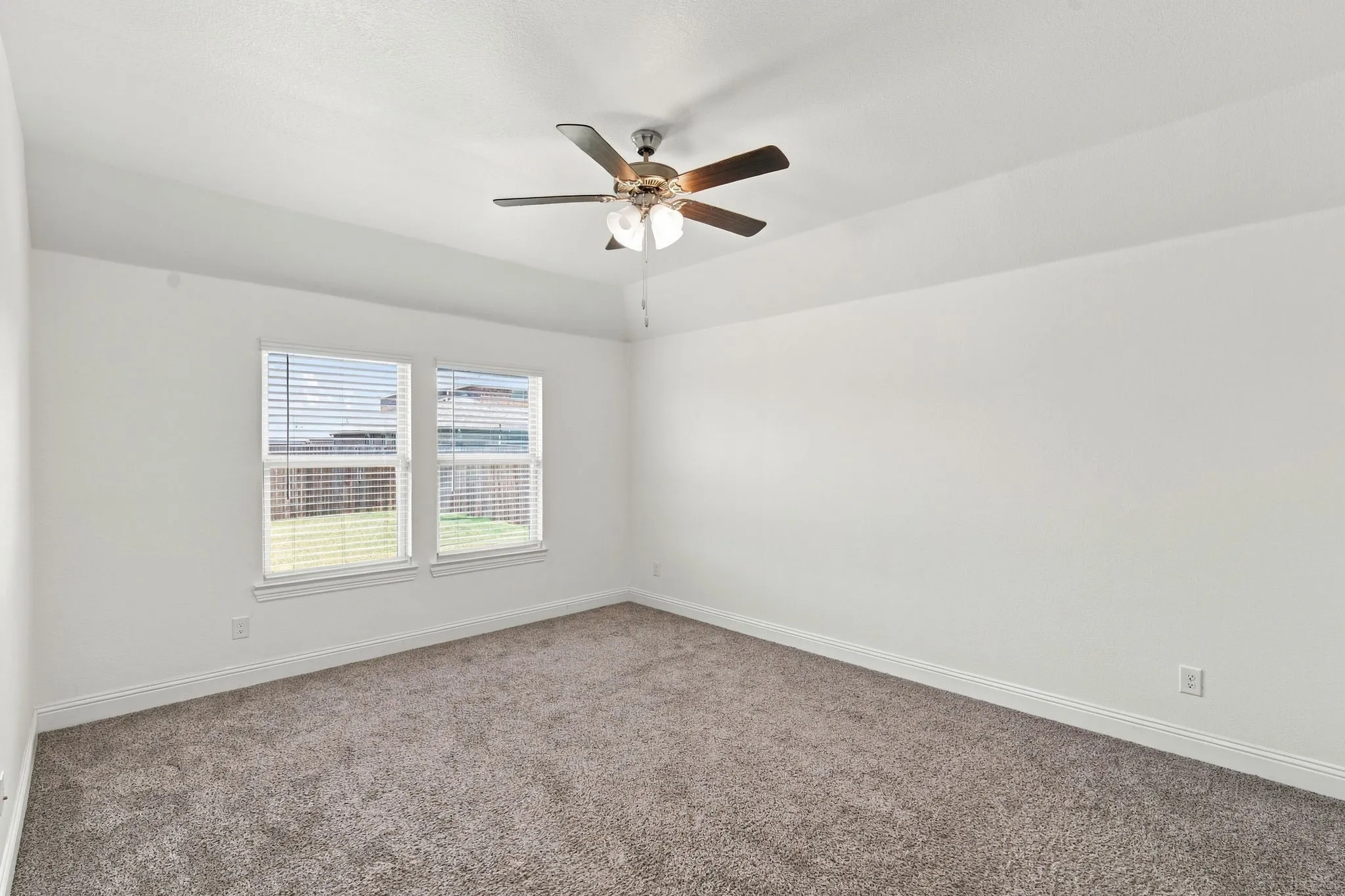 Vaulted ceiling with a ceiling fan, dual windows with blinds, and neutral carpeting