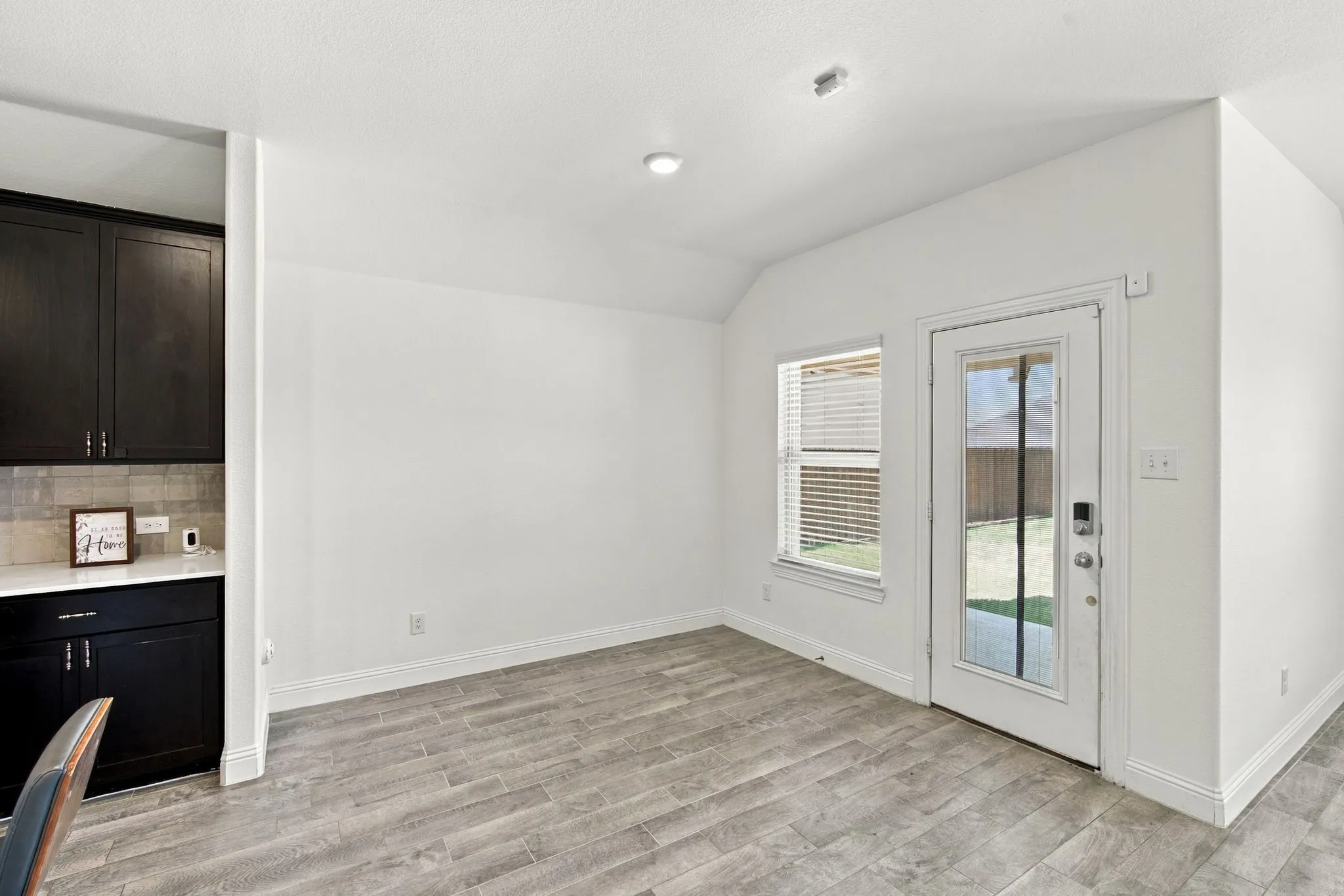 Wood-finish flooring, white walls, dark cabinetry, light-toned backsplash, and a glass-paneled exterior door