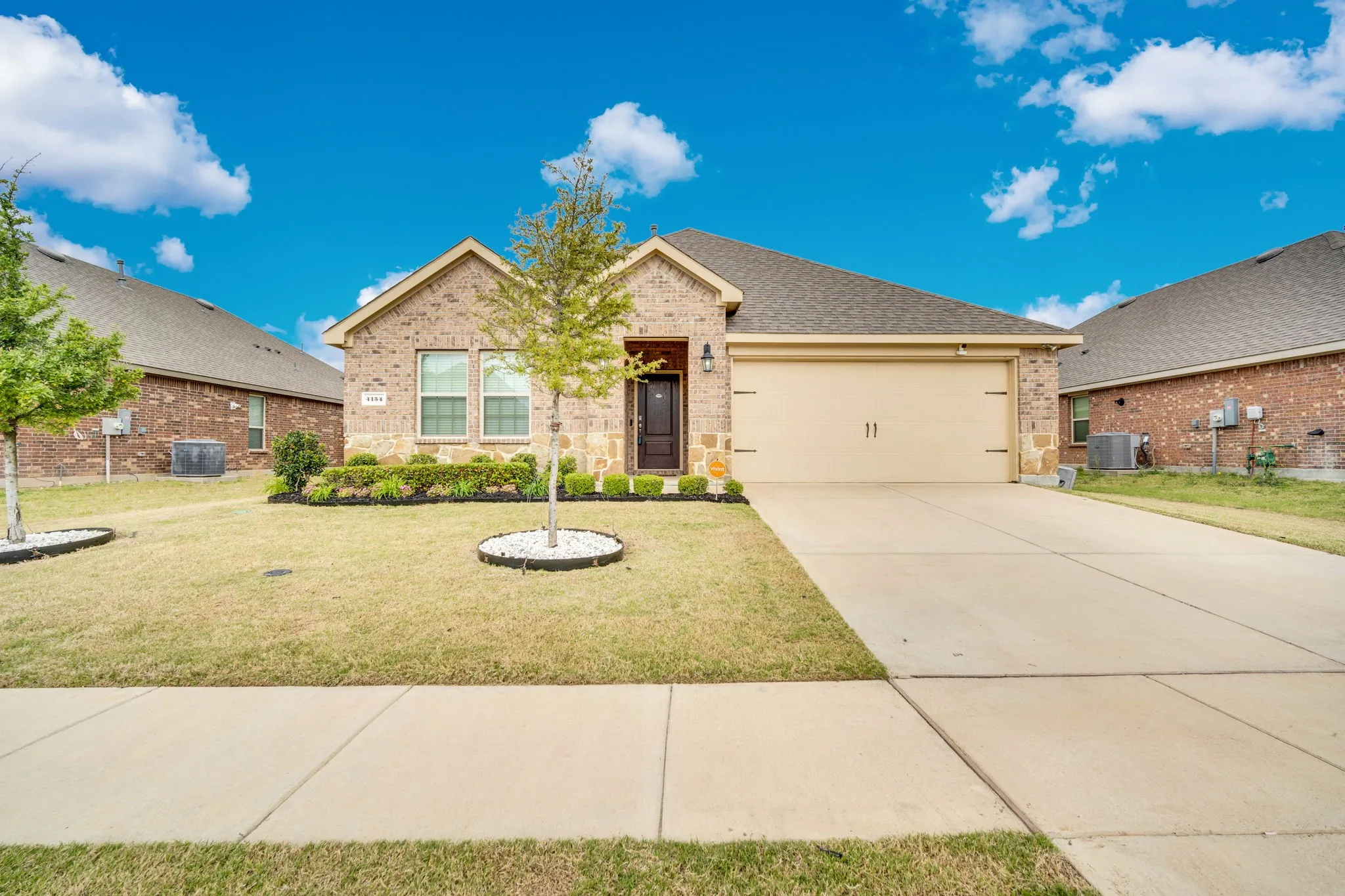 Brick veneer exterior with a concrete driveway, attached garage, and mature landscaping