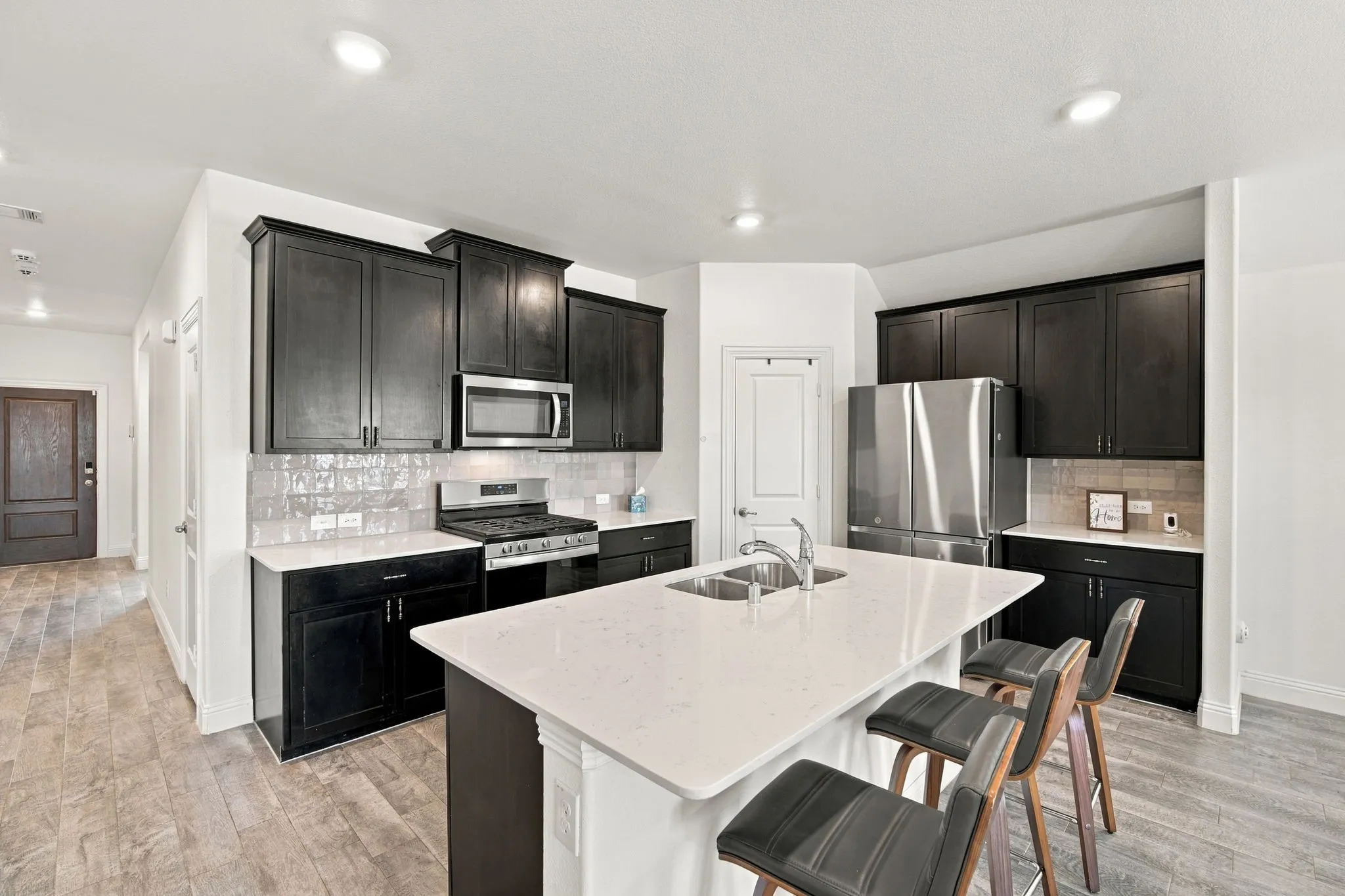 Kitchen featuring dark wood-finish cabinetry, light-toned countertops, stainless steel appliances, a center island with sink, and tile flooring