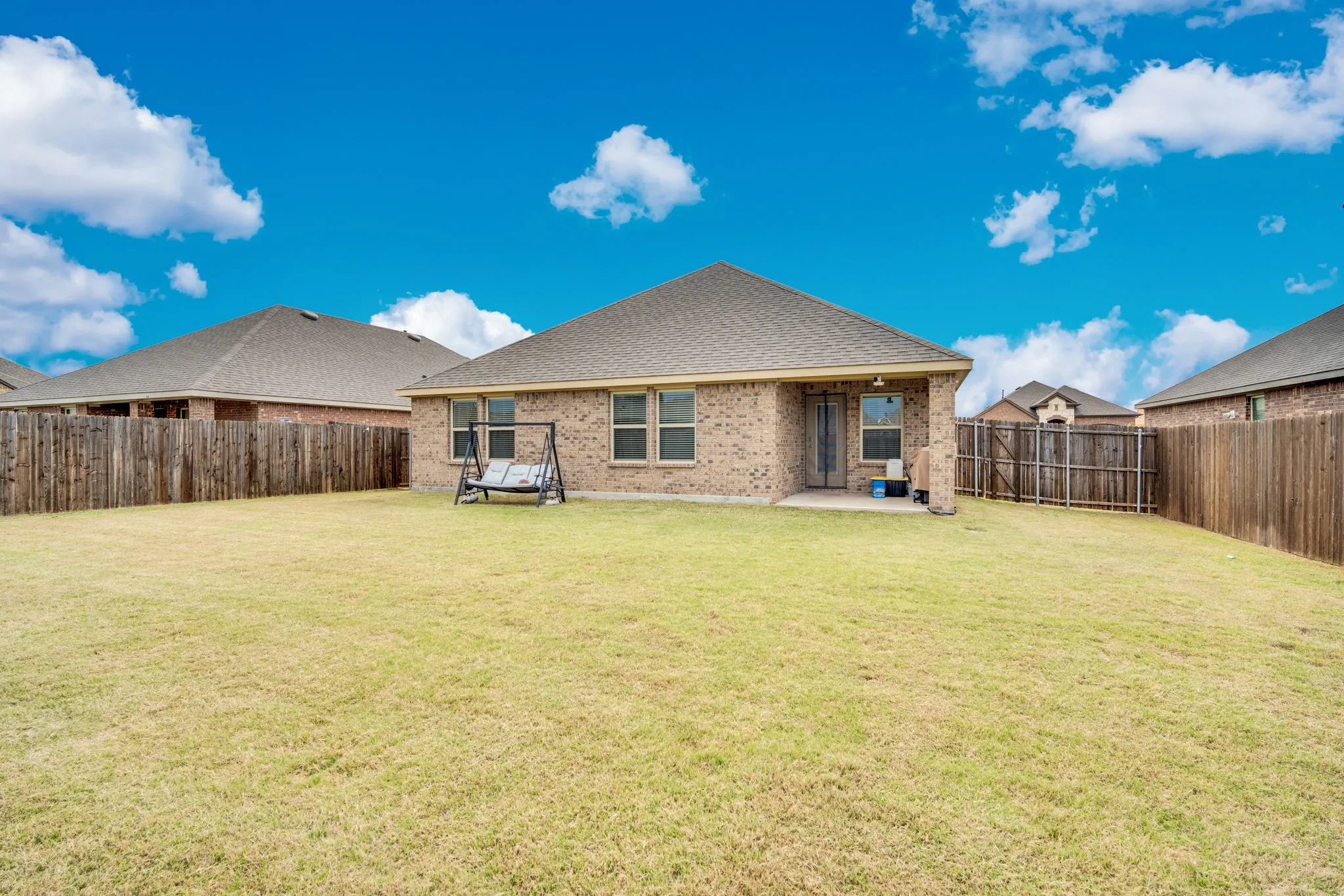 Expansive grassy yard with wood fencing, brick exterior, and covered patio
