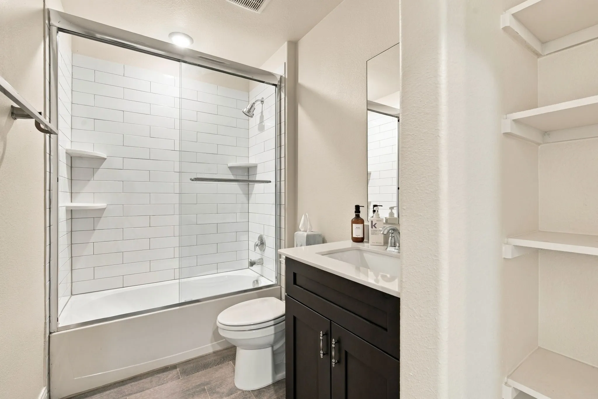 Tub and shower combination with subway tile surround, clear glass enclosure, and built-in shelving
