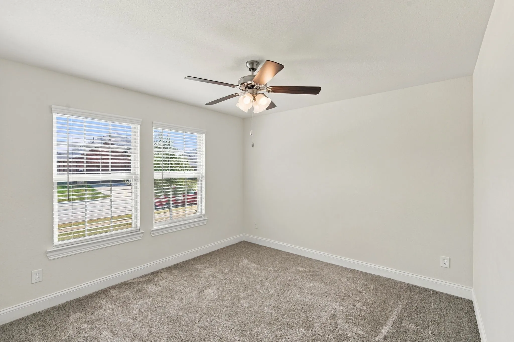 Neutral wall paint, ceiling fan with light fixture, two windows with blinds, and gray carpet flooring