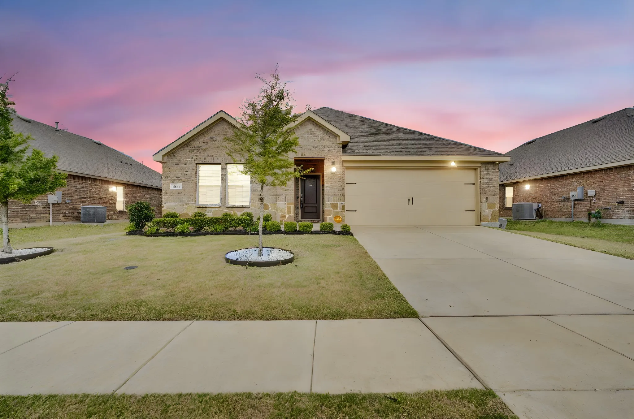 Brick and stone facade, attached two-car garage, manicured lawn, front landscaping, and a concrete driveway