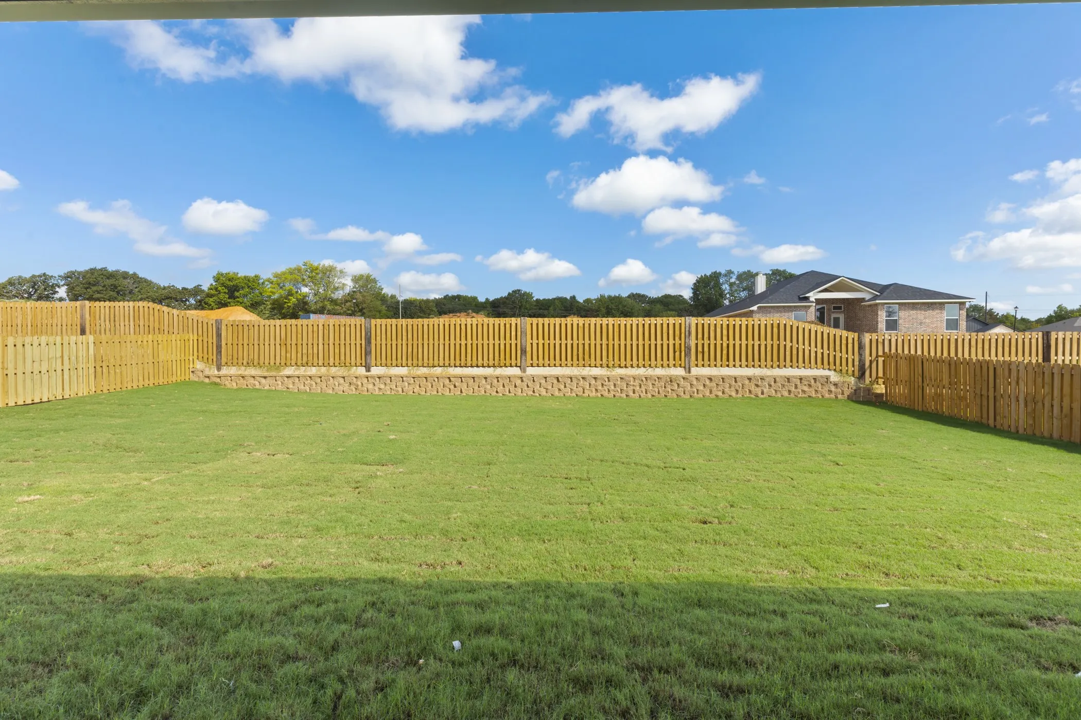 Expansive backyard featuring a lush lawn, wood privacy fencing, and a retaining wall
