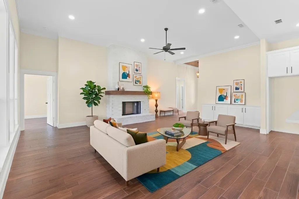Spacious living area featuring wood-finish flooring, a white brick fireplace with a wood mantle, built-in cabinetry, and a ceiling fan