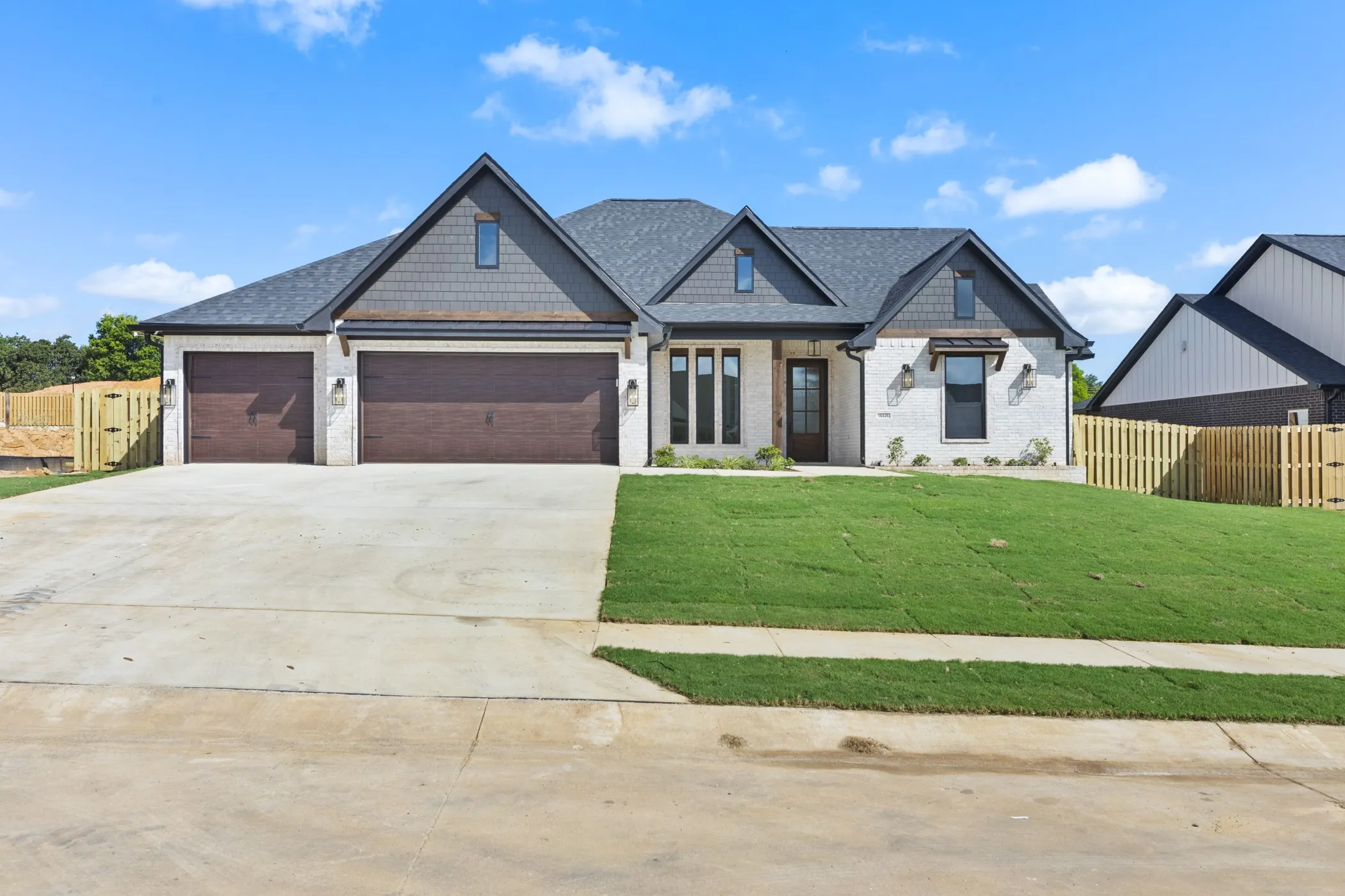Modern farmhouse exterior with white brick and dark shingle siding, a three-car garage, and a newly installed lawn