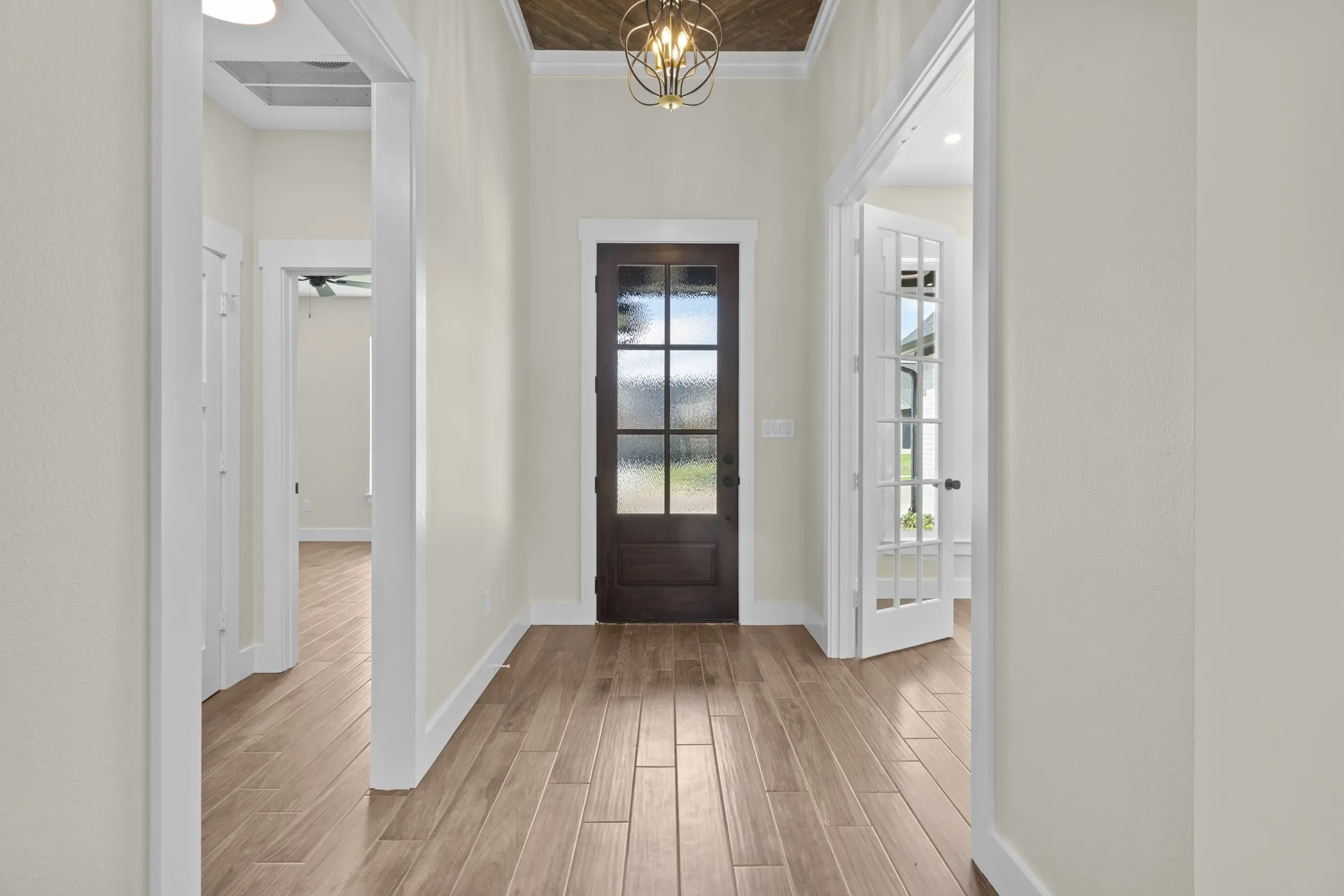 Wood-finish flooring, dark wood entry door with frosted glass, coffered ceiling with wood paneling, decorative ceiling light fixture, and white French doors