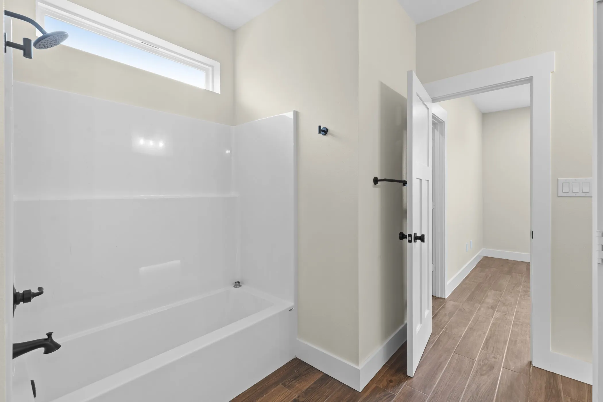 White bathtub with a shower, transom window, dark bronze showerhead, dark bronze faucet, and wood-finish flooring