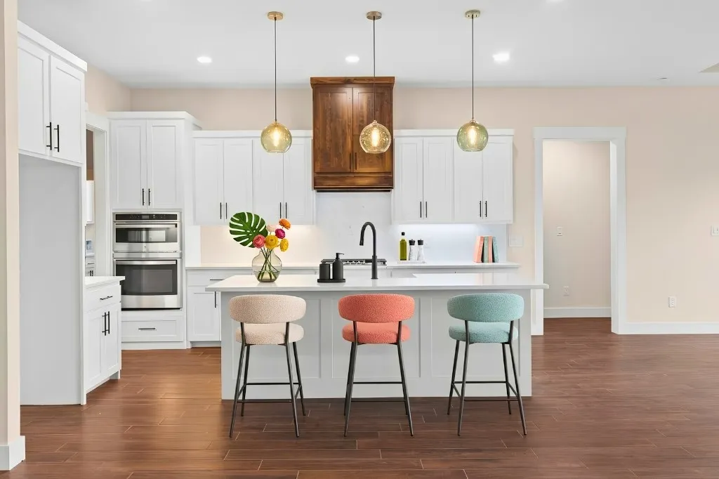 Kitchen featuring white cabinetry, built-in stainless steel appliances, a center island with sink, three pendant lights, and wood-finish flooring