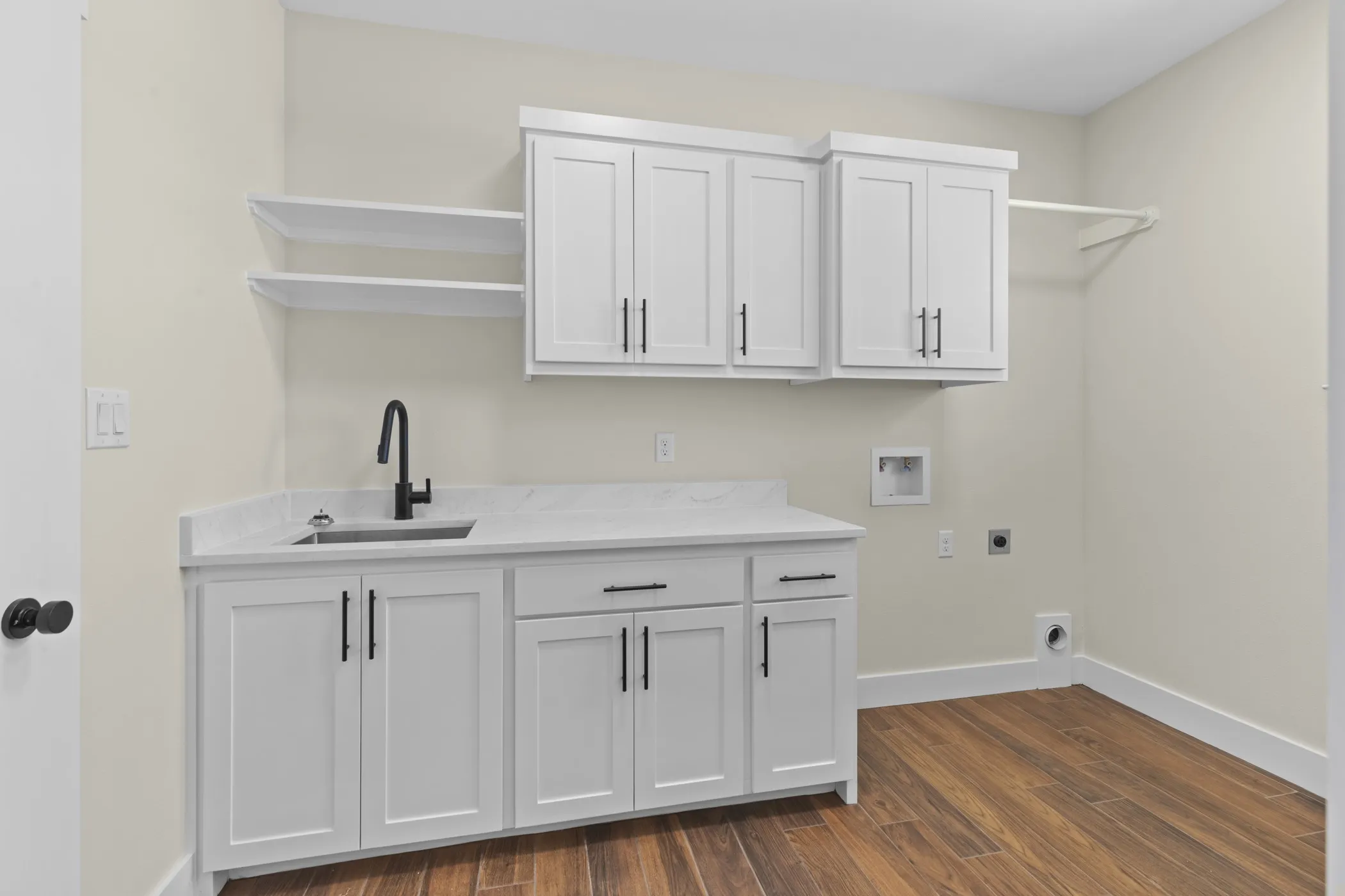 White shaker cabinetry, stone-finish countertop, undermount sink with a matte black faucet, and wood-finish flooring
