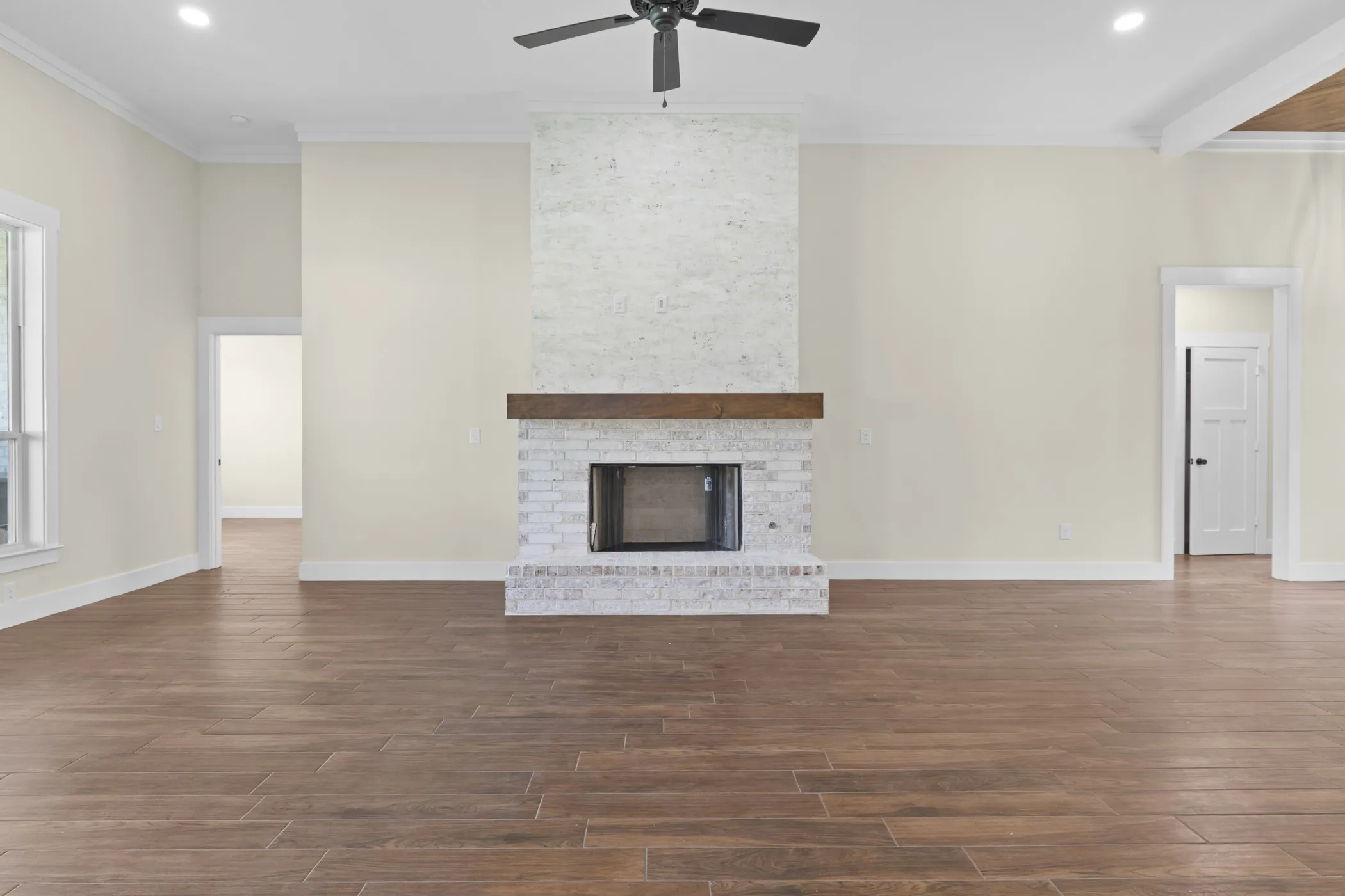 Spacious living area featuring wood-finish flooring, a white brick fireplace with a wood mantle, a ceiling fan, and recessed lighting