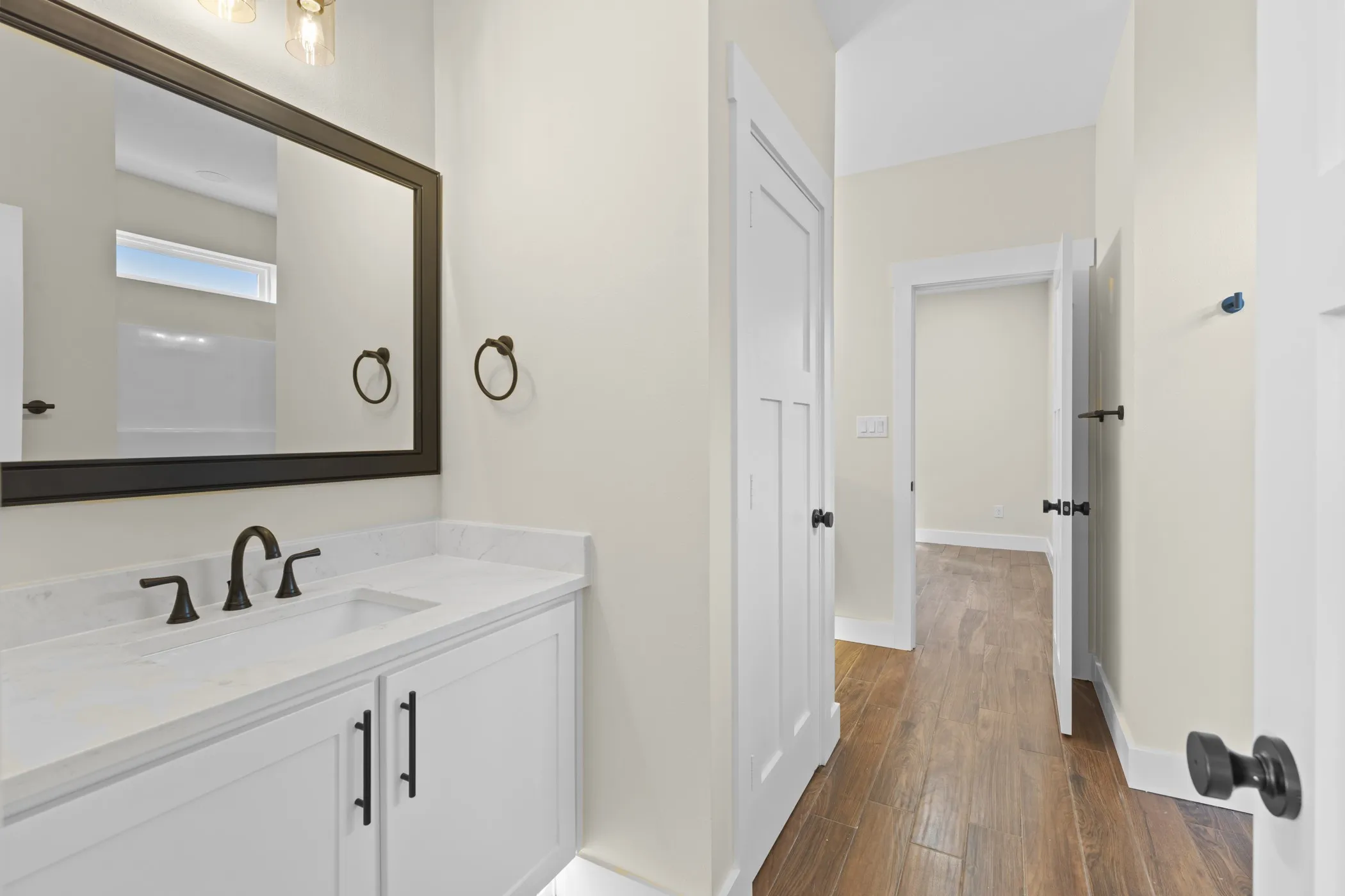 White vanity with integrated sink, black hardware, framed mirror, and wood-finish flooring