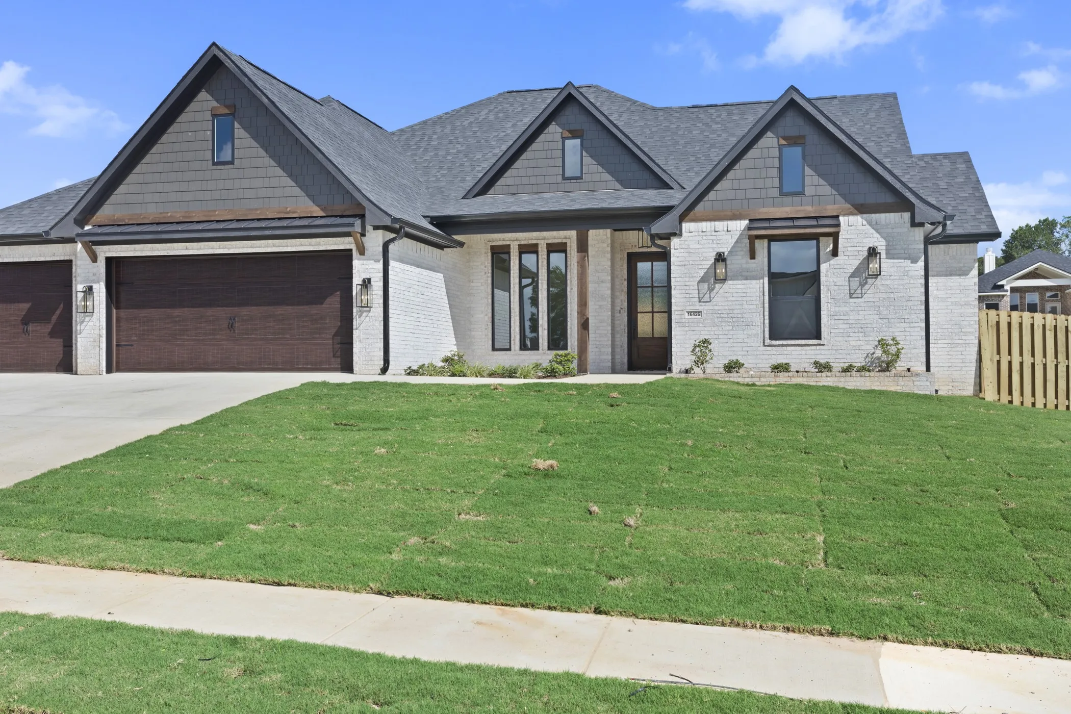 Modern exterior featuring white brick, dark shingle roof, wood-look garage doors, and black-framed windows