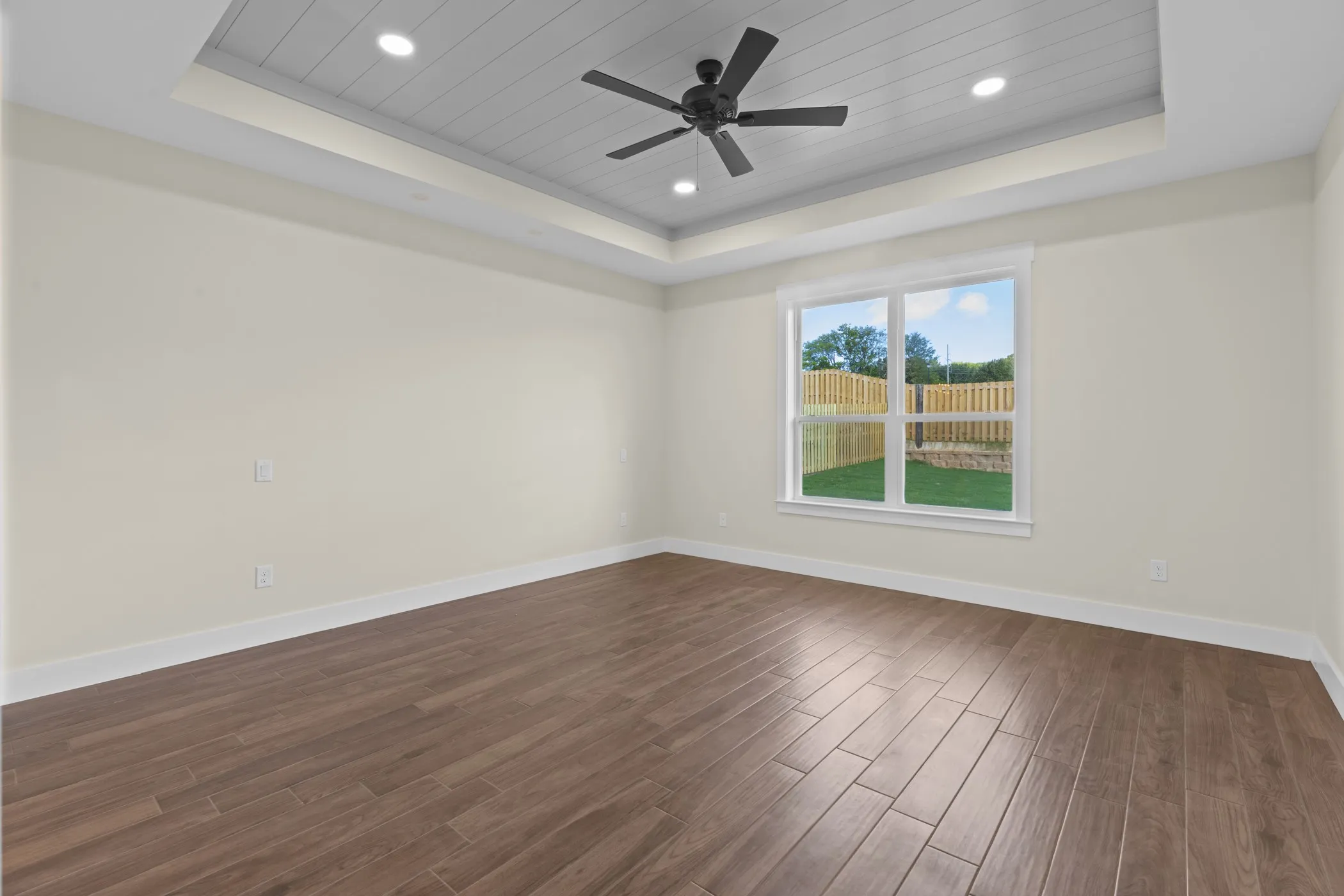 Tray ceiling with recessed lighting and a ceiling fan, wood-finish flooring, and a large window