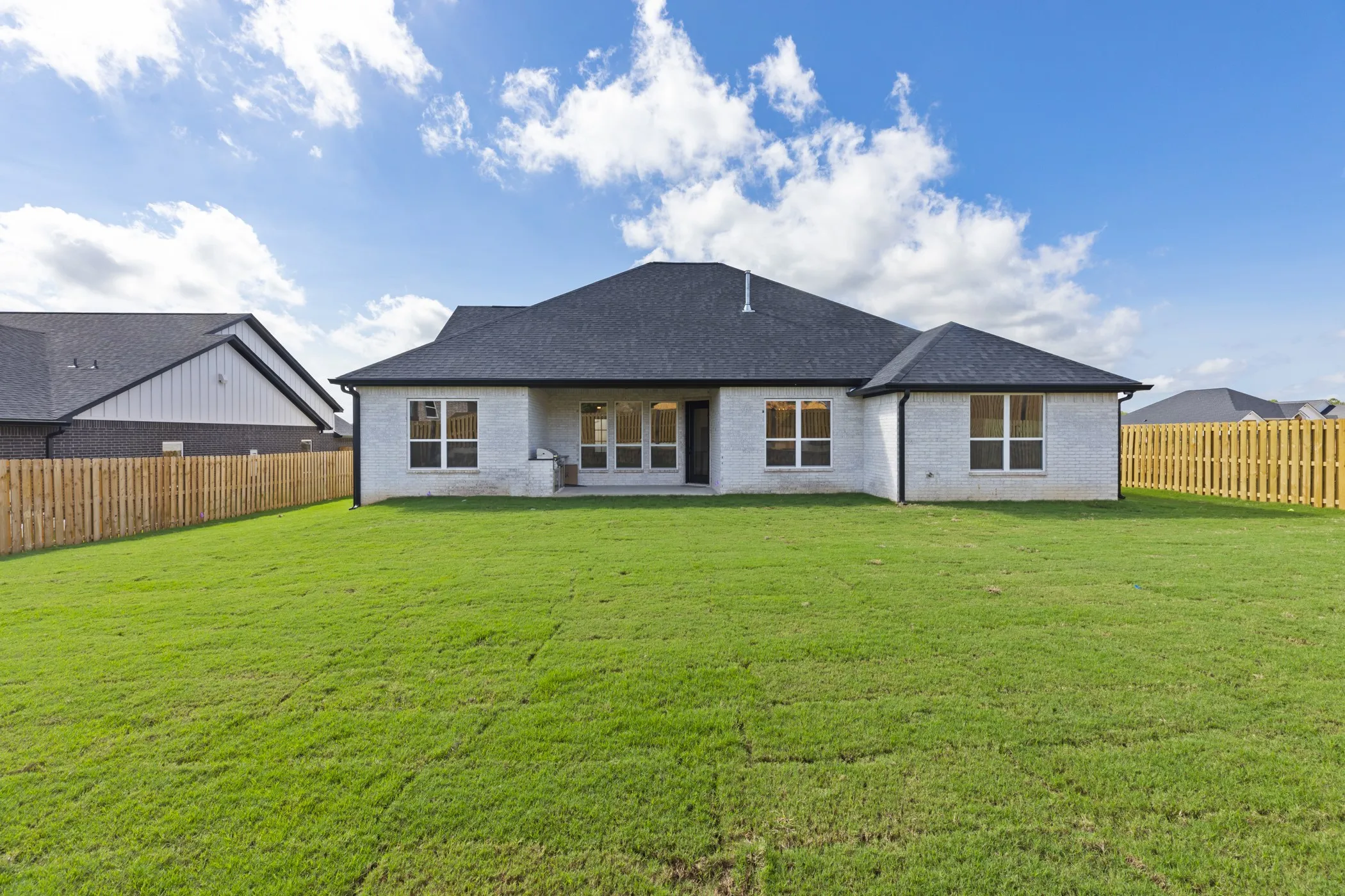 Expansive backyard featuring a manicured lawn, full privacy fencing, and a white brick exterior
