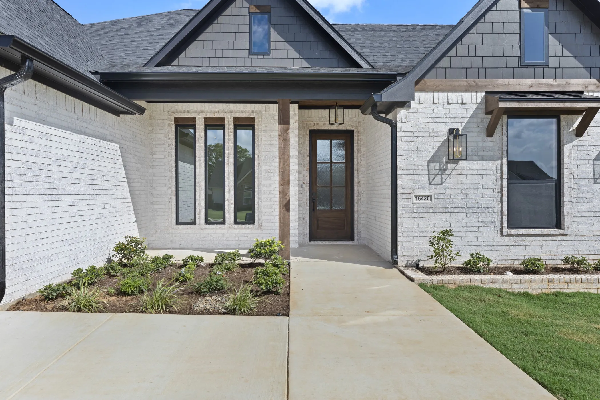 White brick exterior with dark trim, shake siding accent, black-framed windows, and a wood-paneled front door