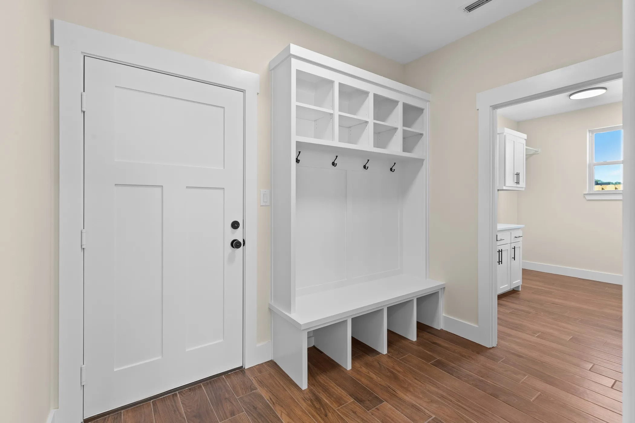 Built-in storage bench with coat hooks and overhead cubbies, wood-finish flooring, and a flat-panel door