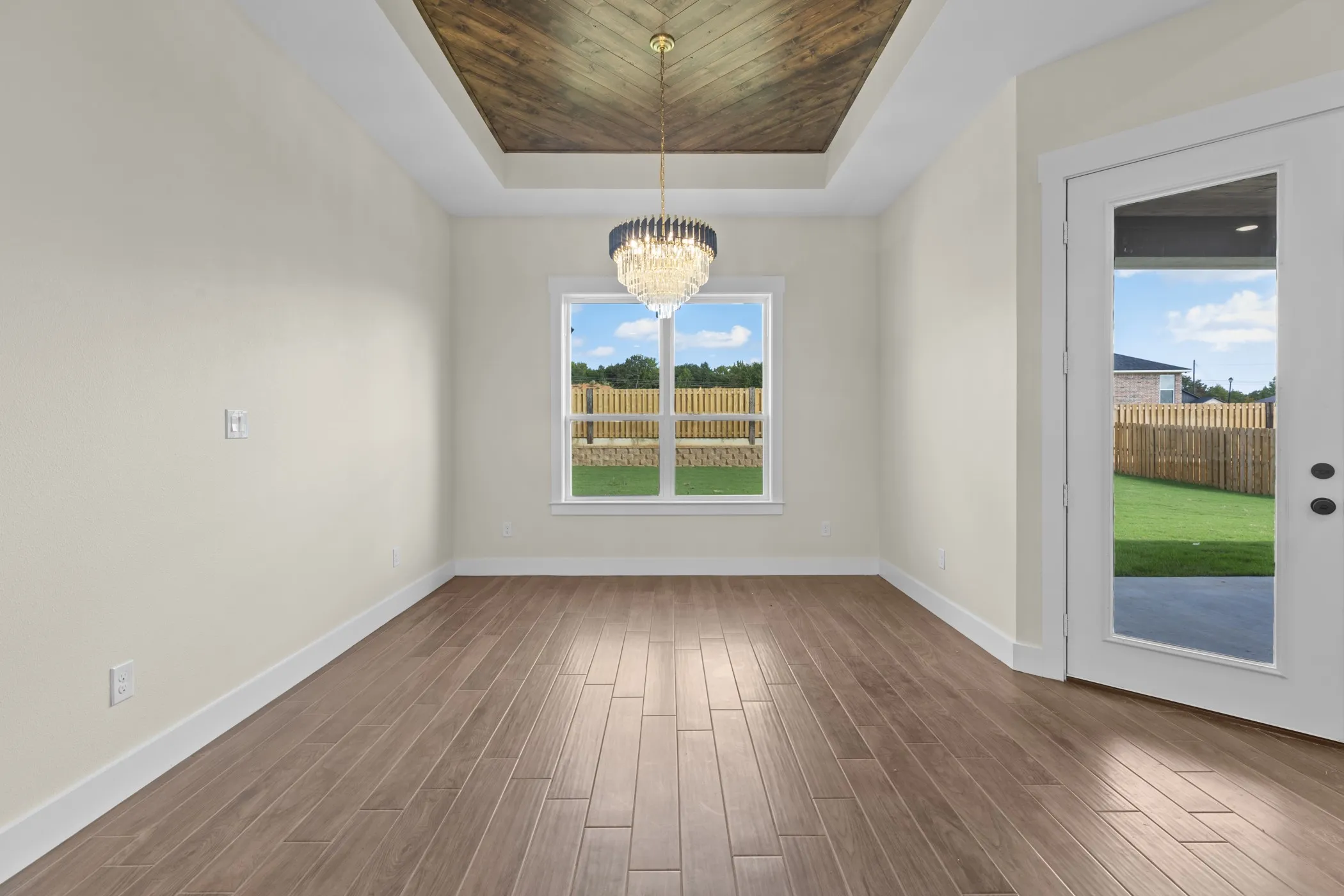 Tray ceiling with wood-finish inlay, large window, wood-finish flooring, and glass-paneled door