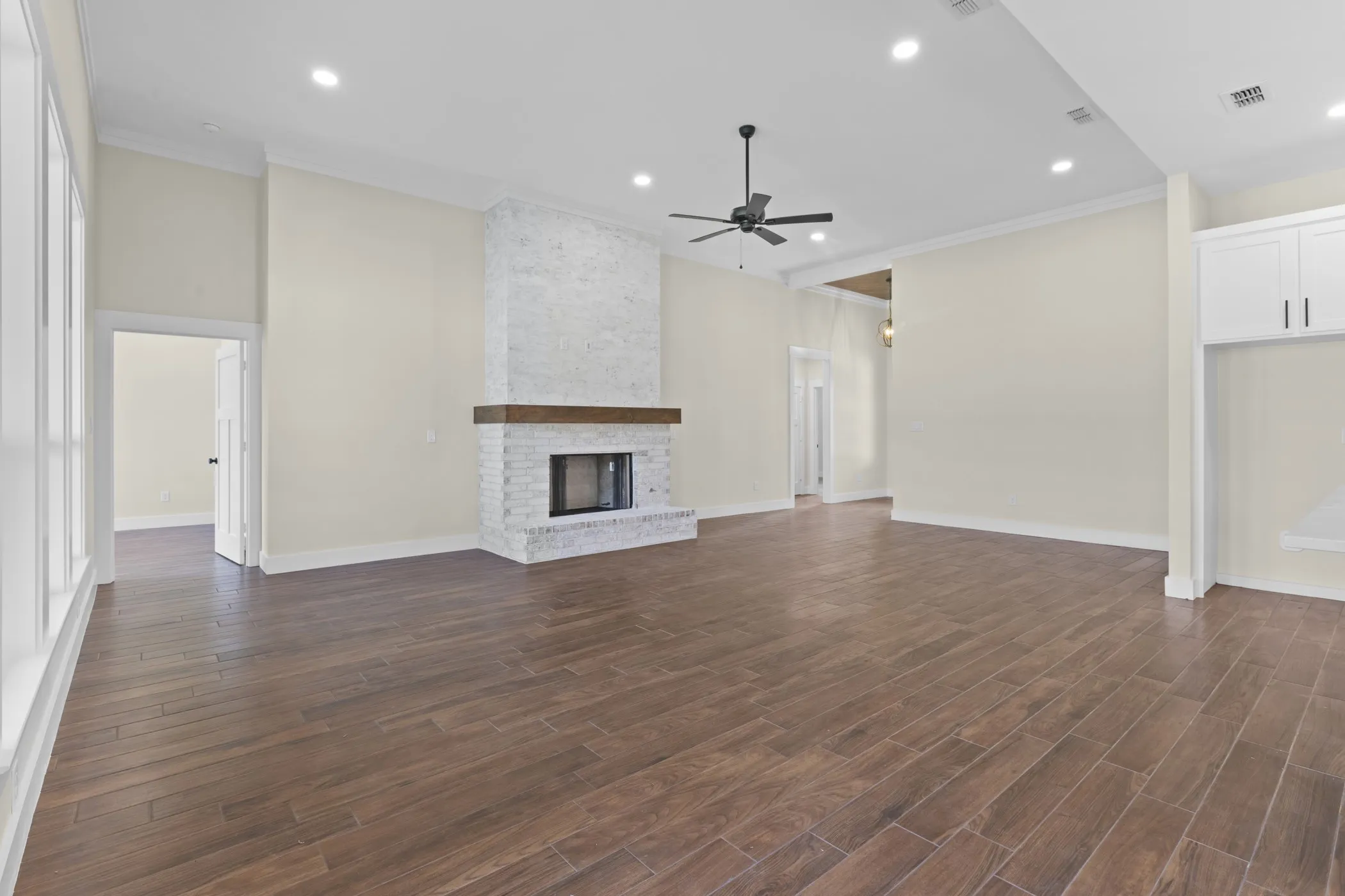 Expansive room with wood-finish flooring, a white brick fireplace with a wood mantle, and recessed lighting