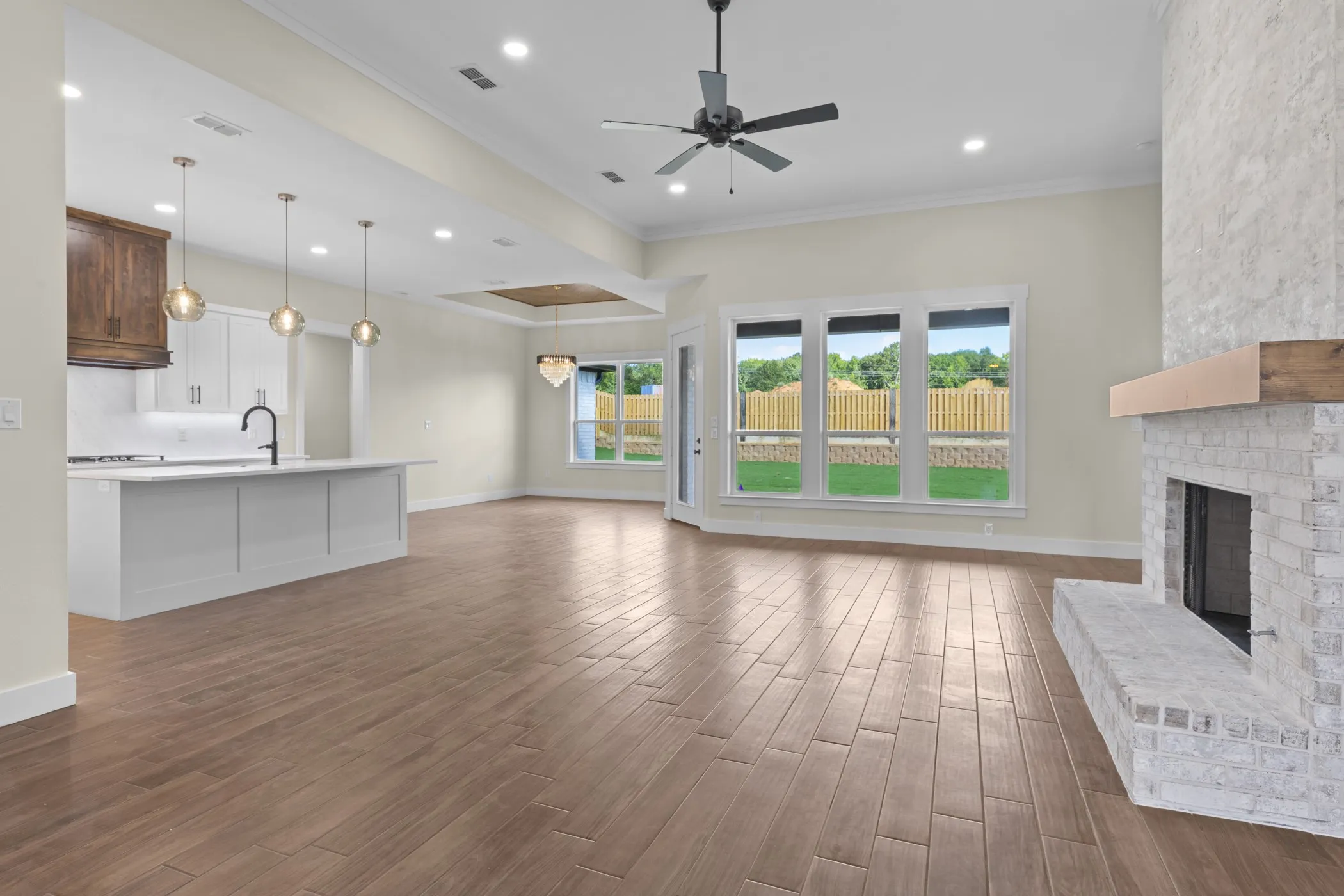 Open-concept living space featuring wood-finish flooring, a white brick fireplace with a wood mantel, and an island kitchen with pendant lighting