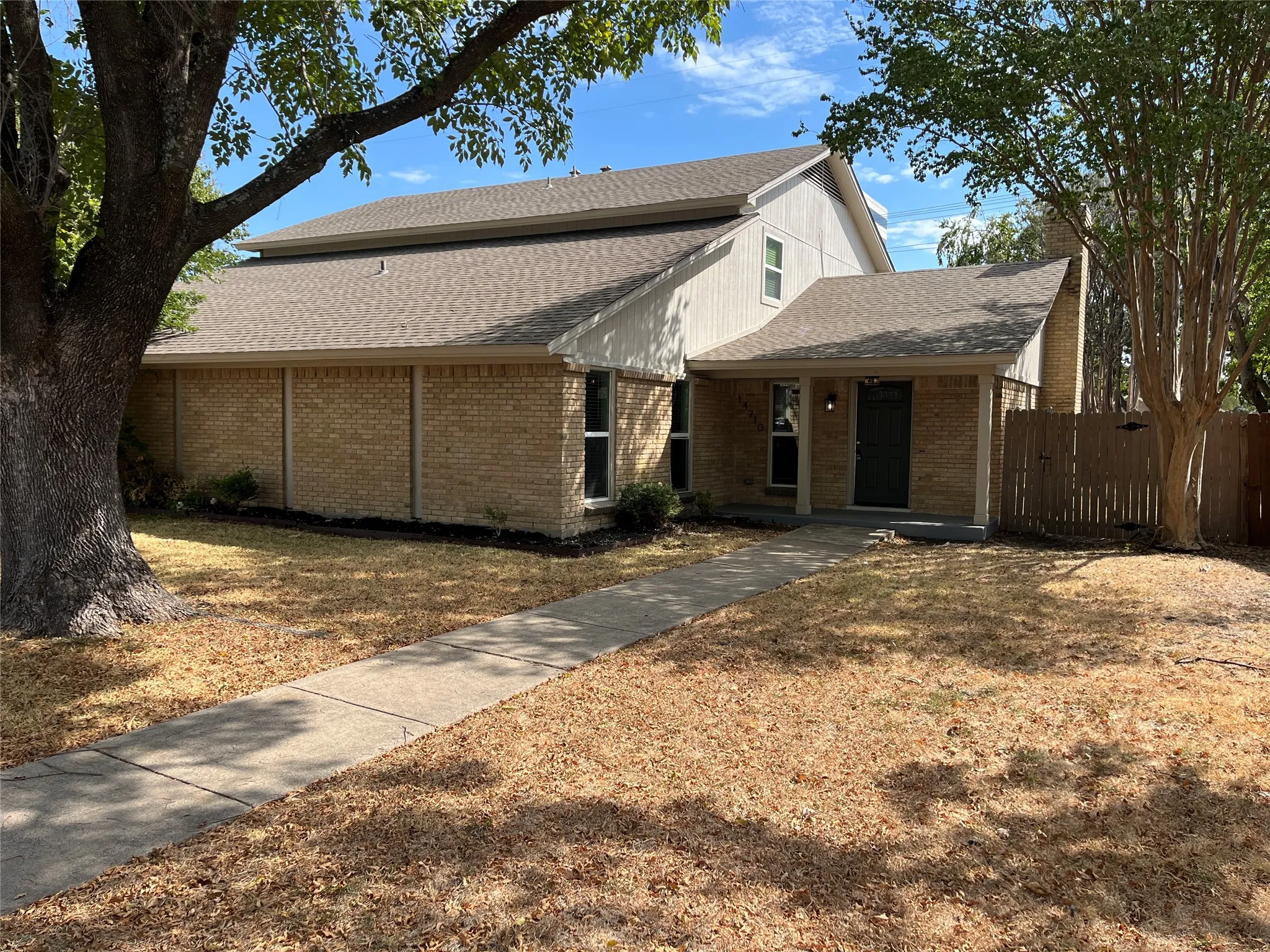 Brick exterior with a covered entry, established landscaping, and a privacy fence