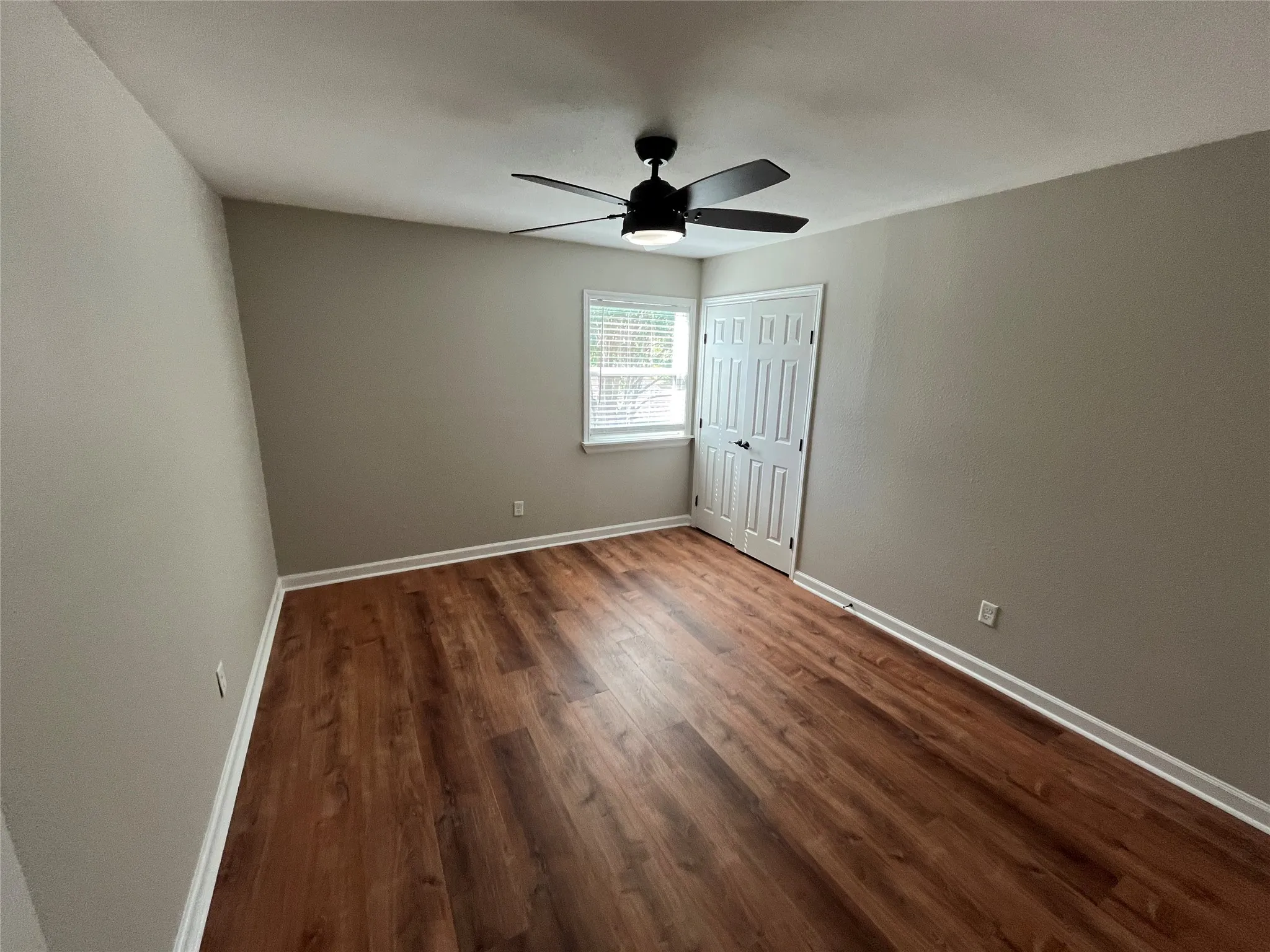 Wood-finish flooring, neutral wall tones, white trim, window with blinds, and ceiling fan with integrated lighting