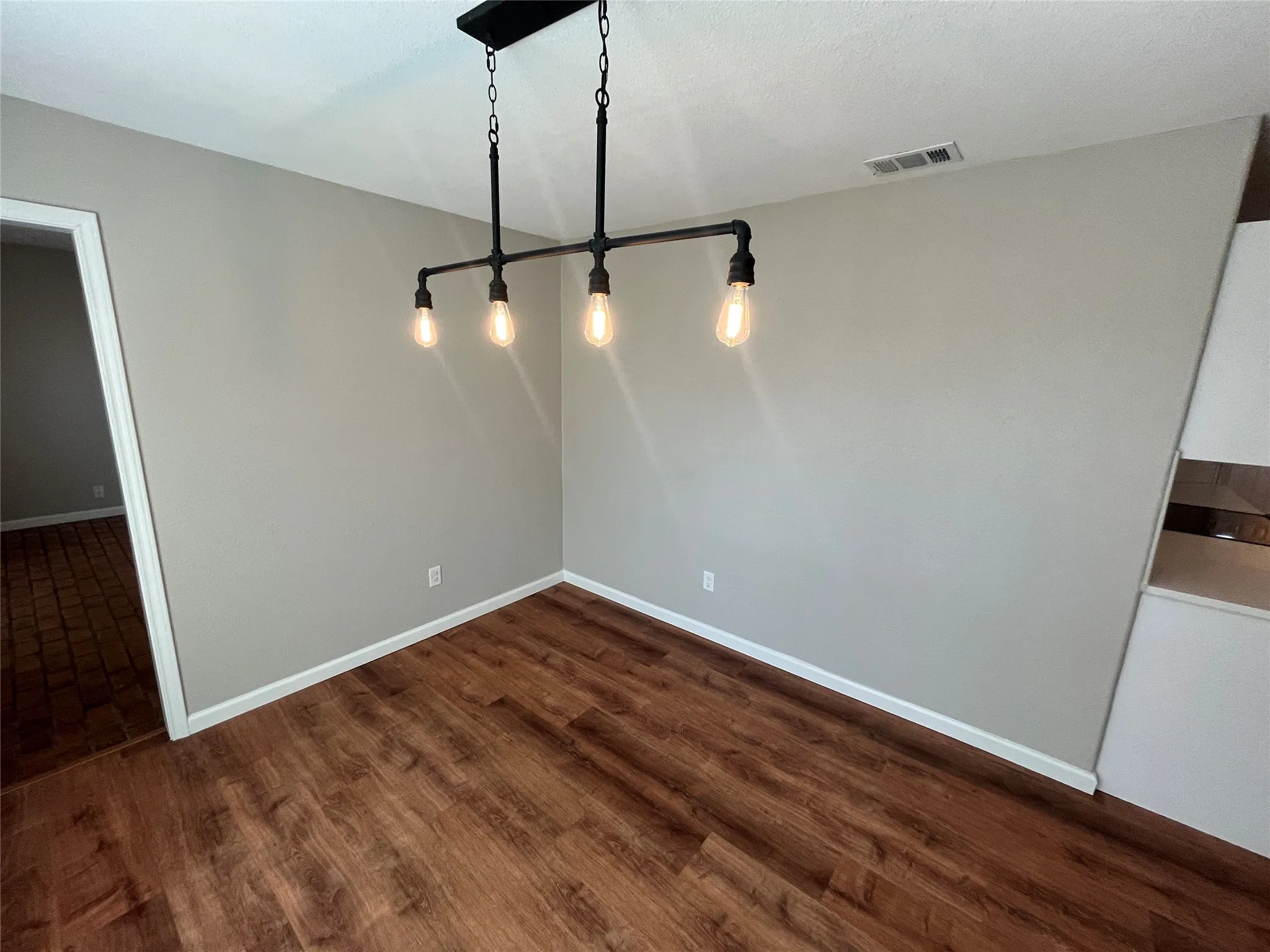 Wood-finish flooring, neutral wall tones, and a linear pendant light fixture