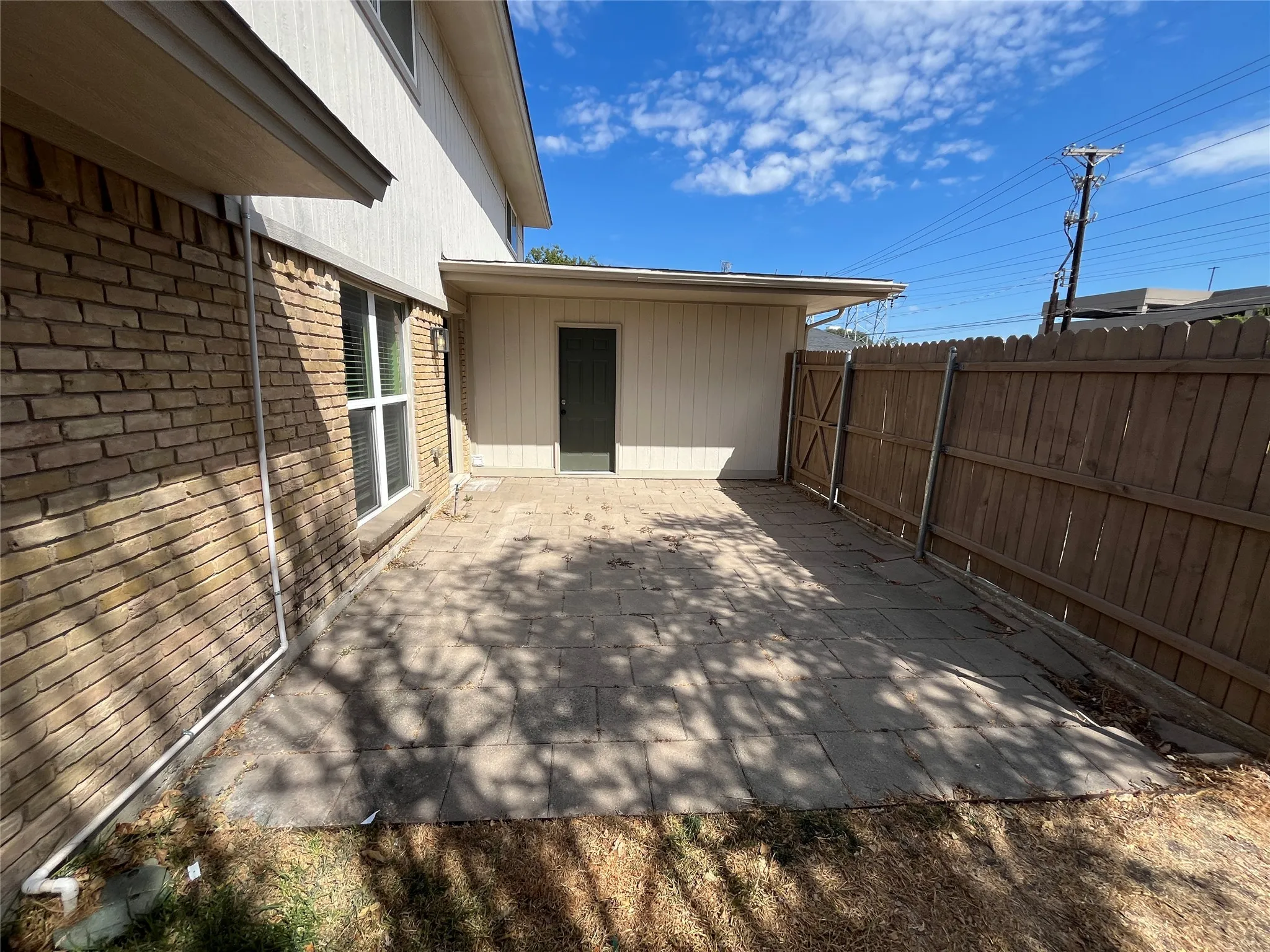 Paved patio area, brick exterior, wood privacy fence, exterior storage structure, and ground-level window