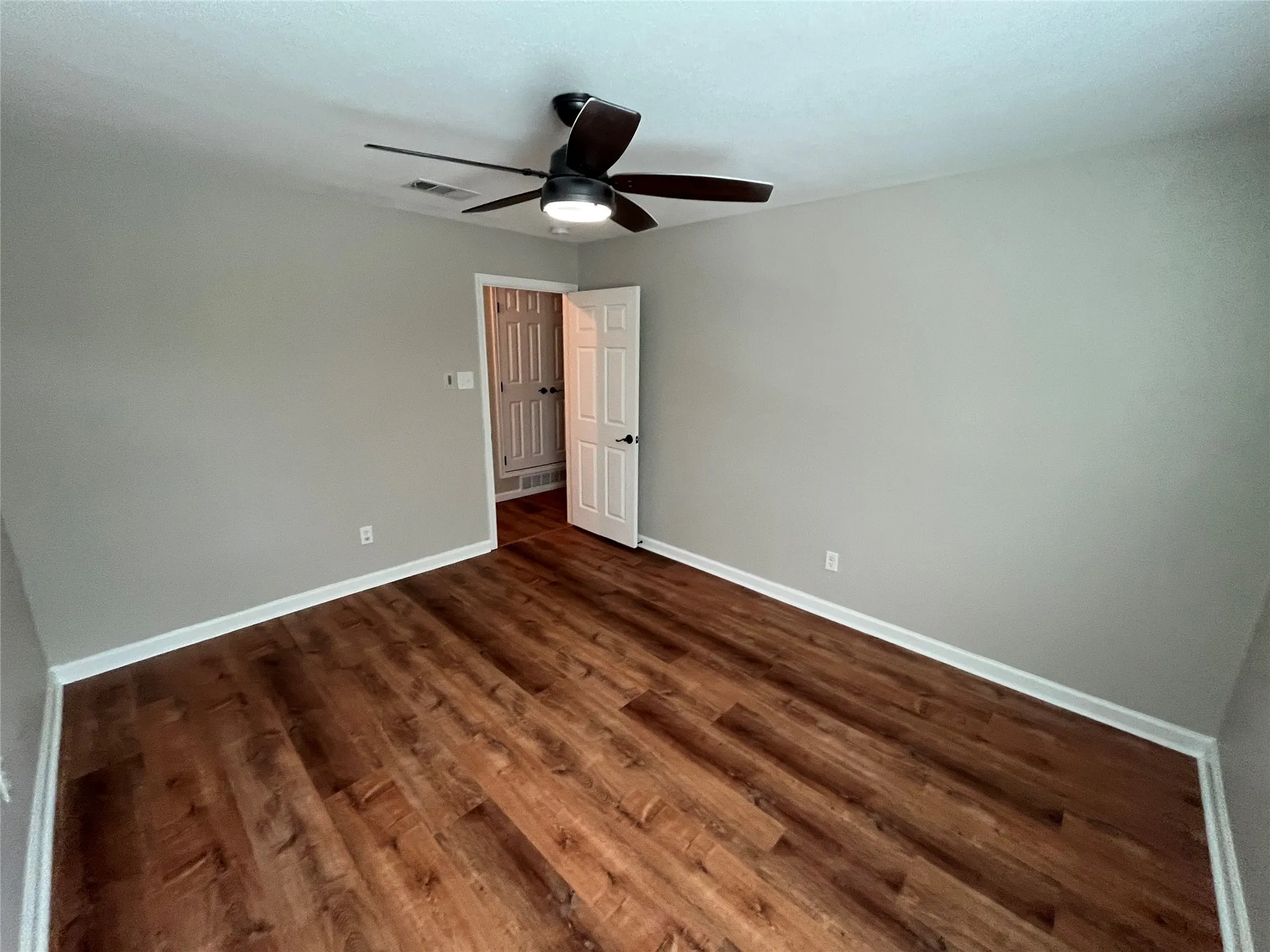 Wood-finish flooring, neutral wall tones, white trim, and a ceiling fan with integrated lighting