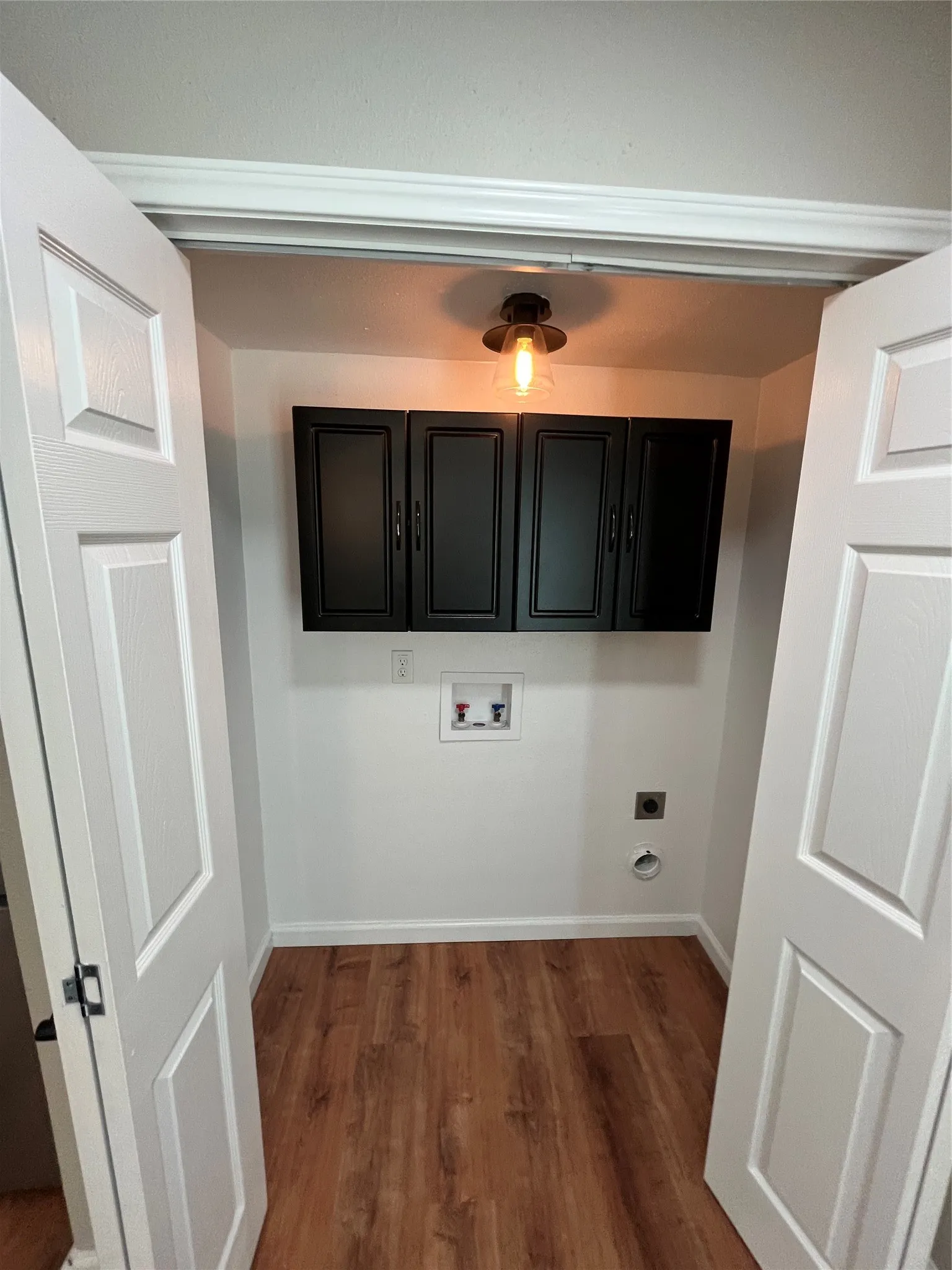 Wood-finish flooring with white baseboards, a ceiling-mounted light fixture, and black upper cabinetry