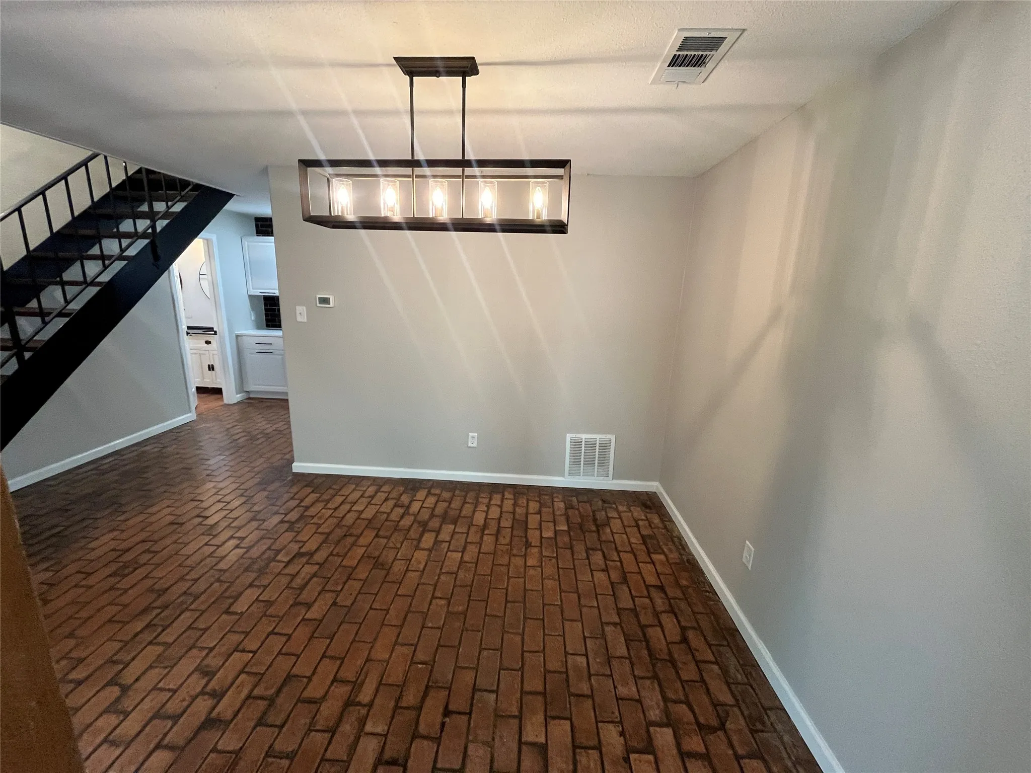 Brick flooring with a black metal handrail staircase and a contemporary linear chandelier