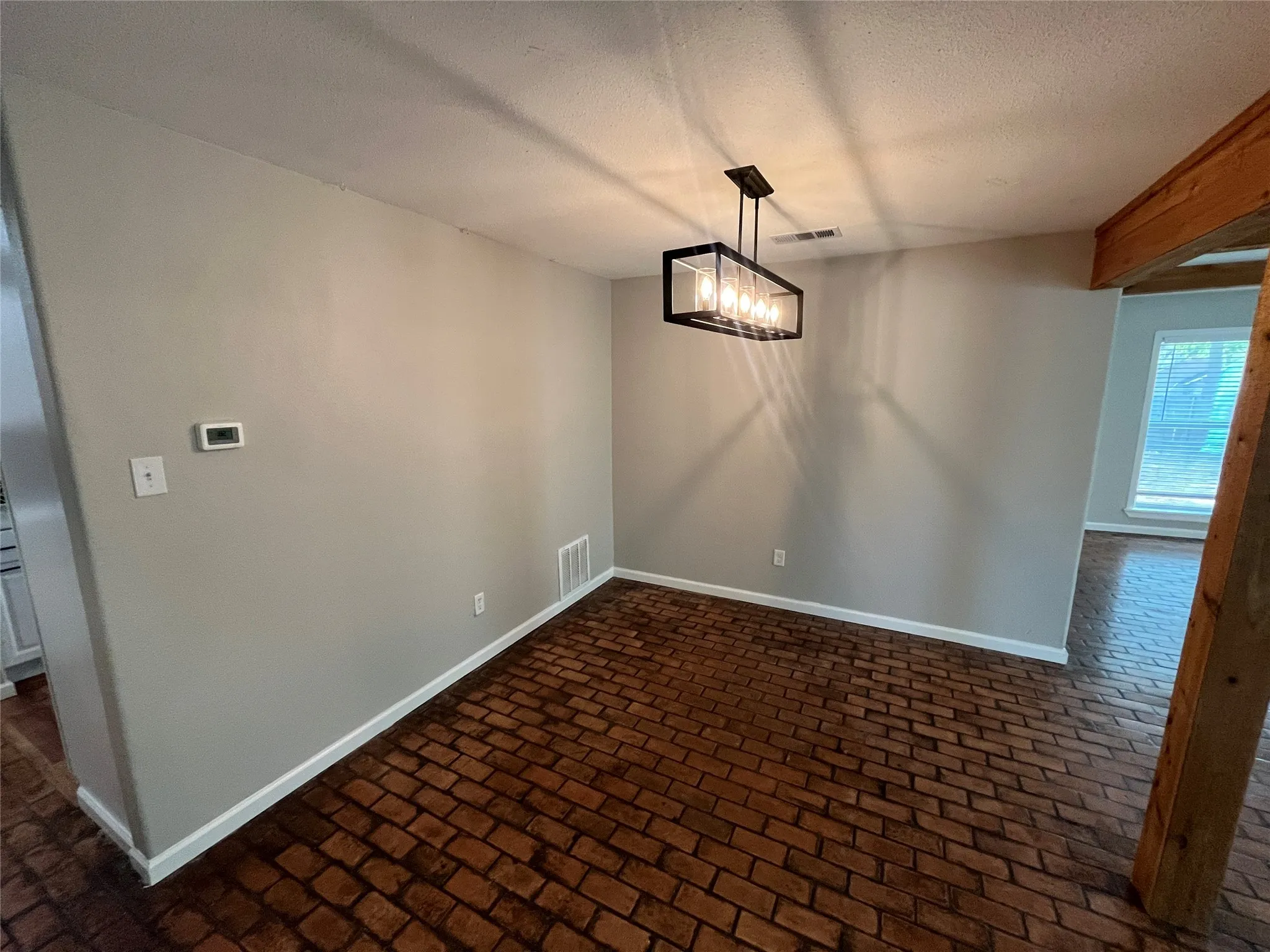 Brick-patterned flooring, ceiling-mounted light fixture, light gray wall finishes, and exposed wood beam