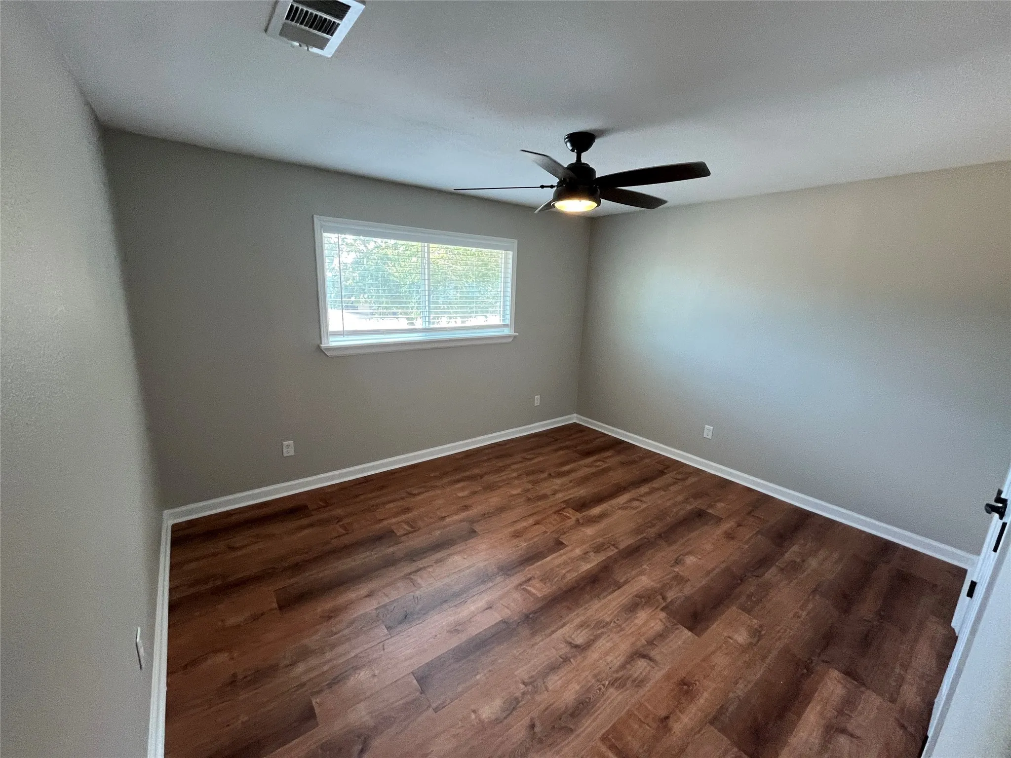 Wood-finish flooring, neutral wall paint, window with blinds, and a ceiling fan with integrated lighting