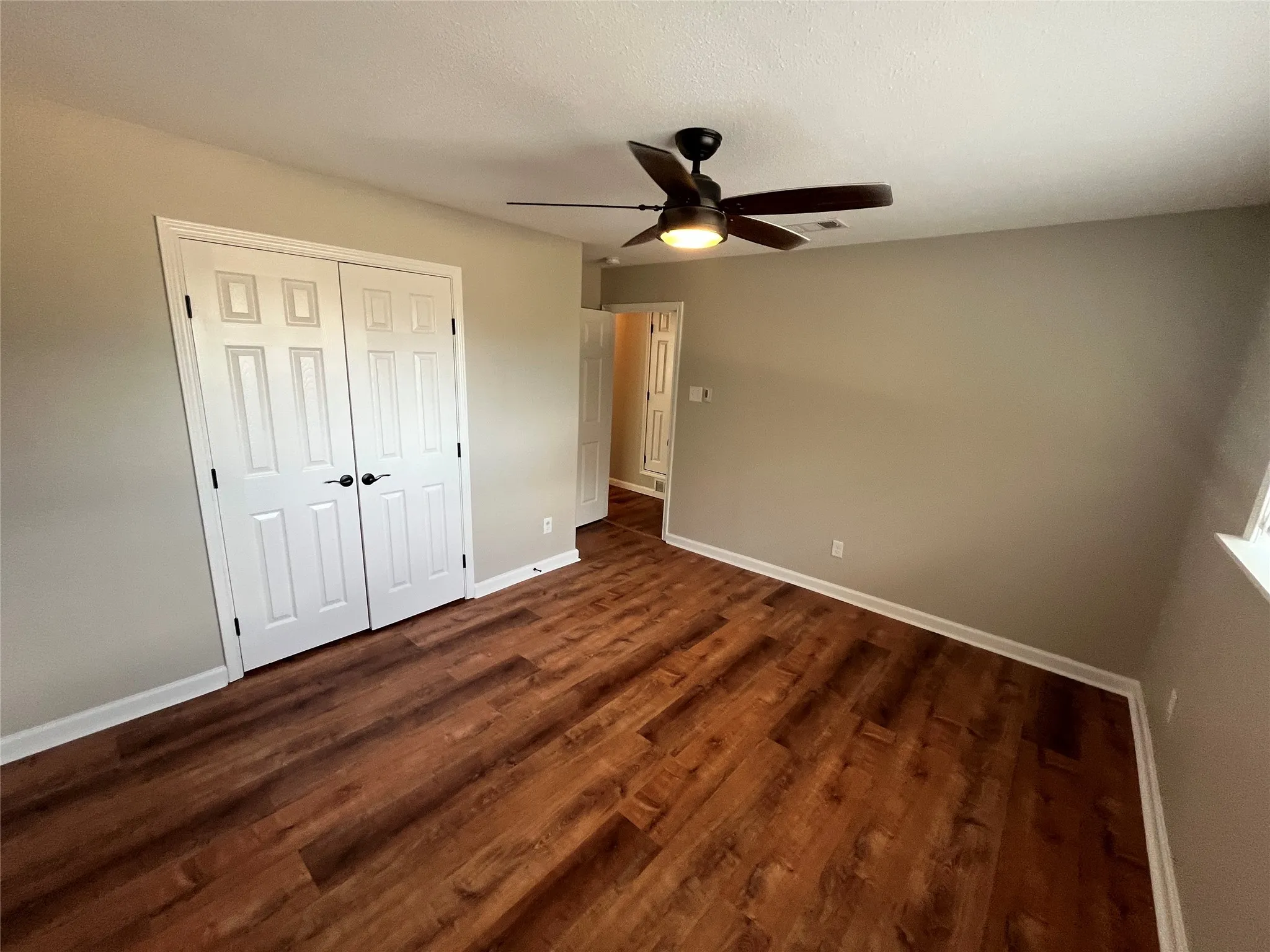 Room featuring wood-finish flooring, a ceiling fan with integrated lighting, and a double-door closet with dark hardware