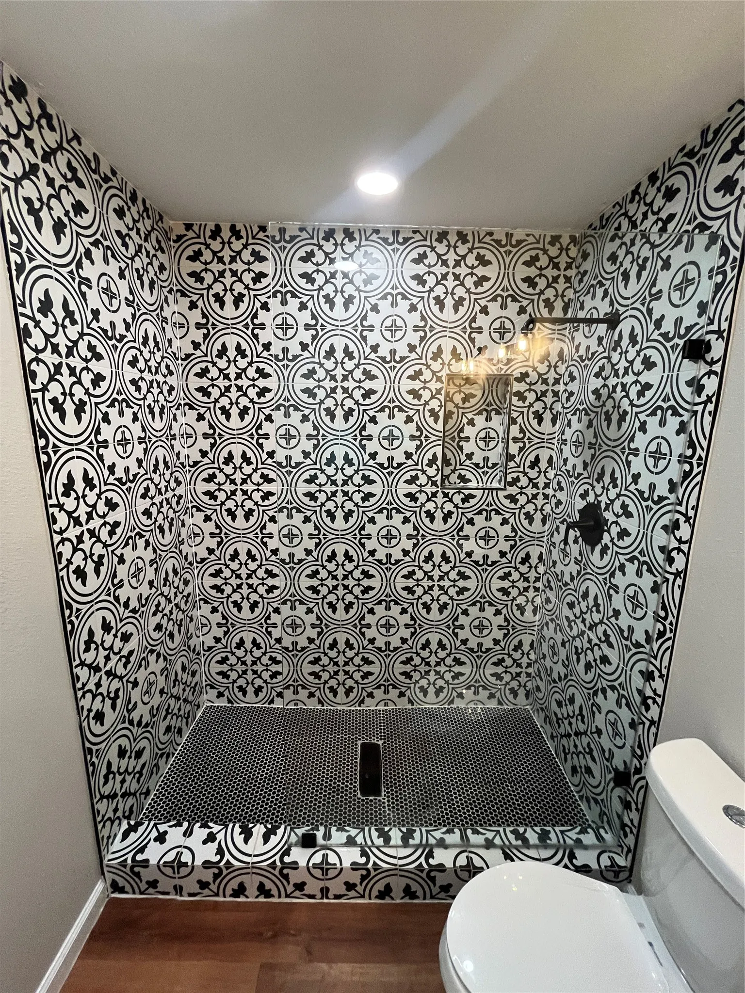 Walk-in shower with black and white patterned tile walls, black mosaic floor tile, and a clear glass enclosure
