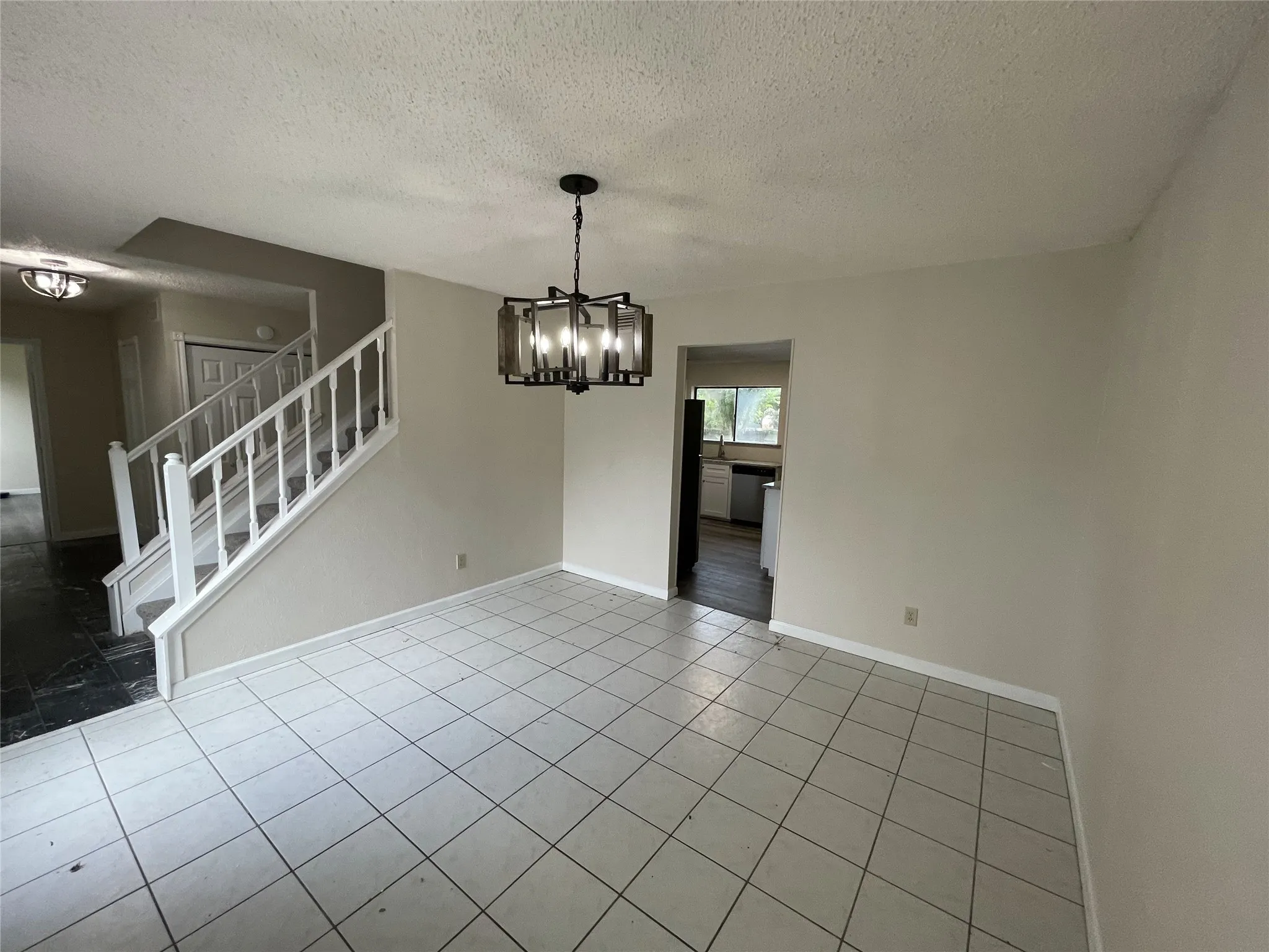 Spacious interior featuring tile flooring, a modern chandelier, and a white staircase with balusters