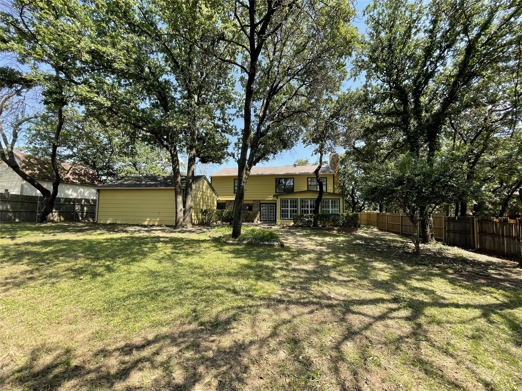 Expansive backyard featuring a lush lawn, mature trees, wood privacy fencing, and a detached structure