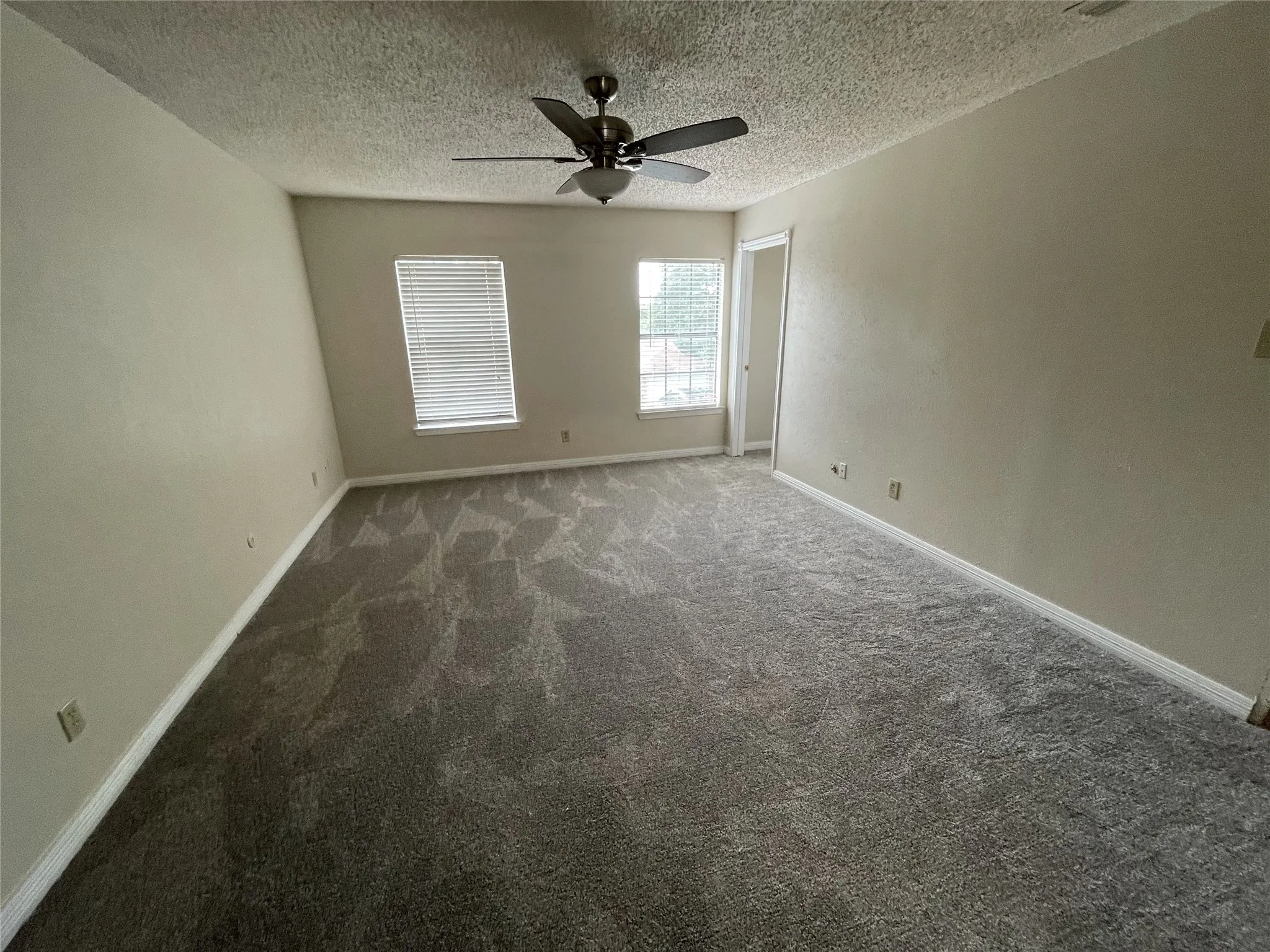 Spacious room featuring patterned carpeting, two windows with horizontal blinds, and a ceiling fan with integrated lighting