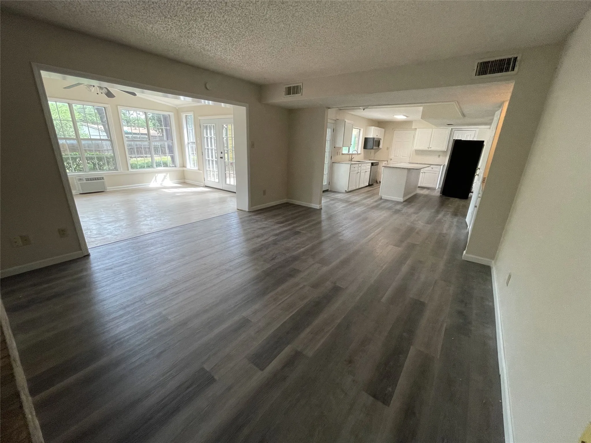 Wood-finish flooring throughout, bright sunroom with multiple windows, kitchen with white cabinetry, stainless steel appliances, and a central island