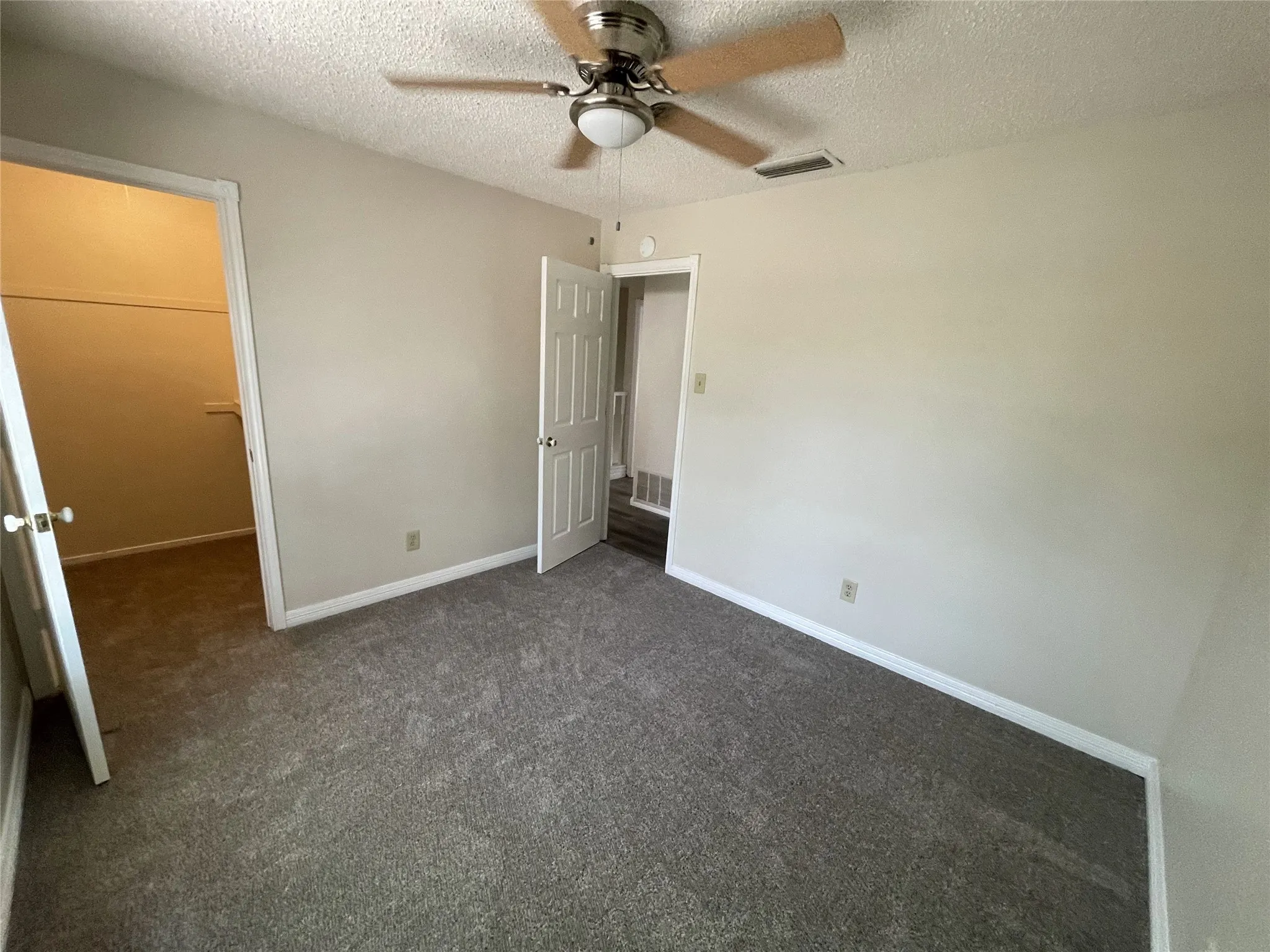 Carpeted room featuring a ceiling fan with integrated lighting, a walk-in closet, and a white paneled door