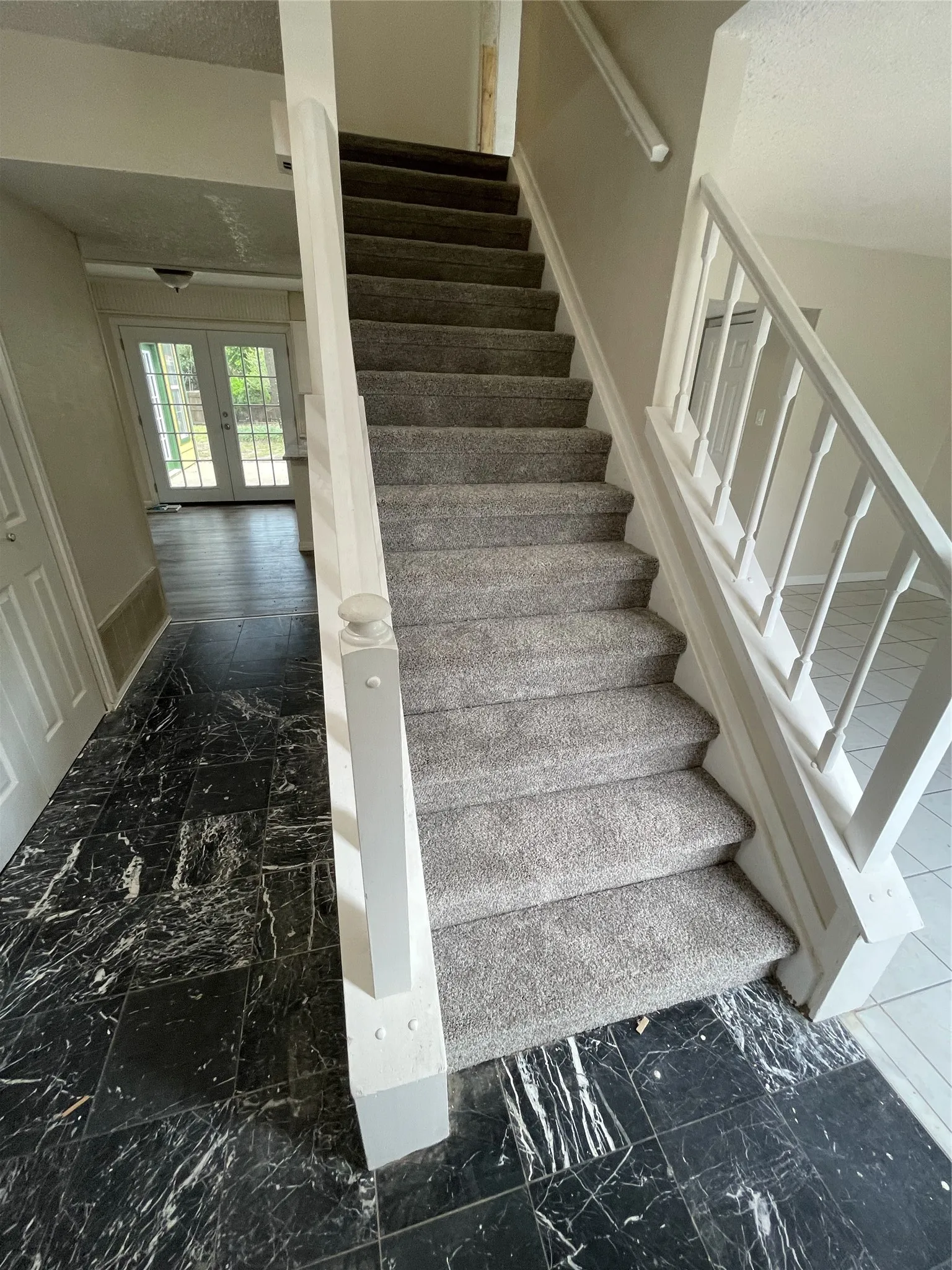 Carpeted stairway with white painted railing, dark patterned tile flooring, and french doors