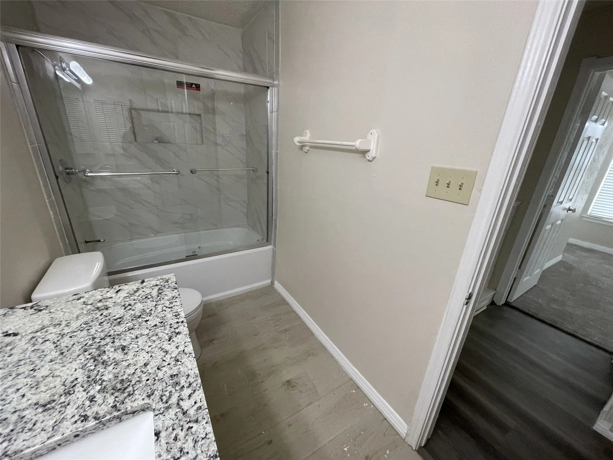 Bathroom featuring a glass-enclosed shower/tub combination with tiled surround, a vanity with a speckled countertop, and wood-finish flooring