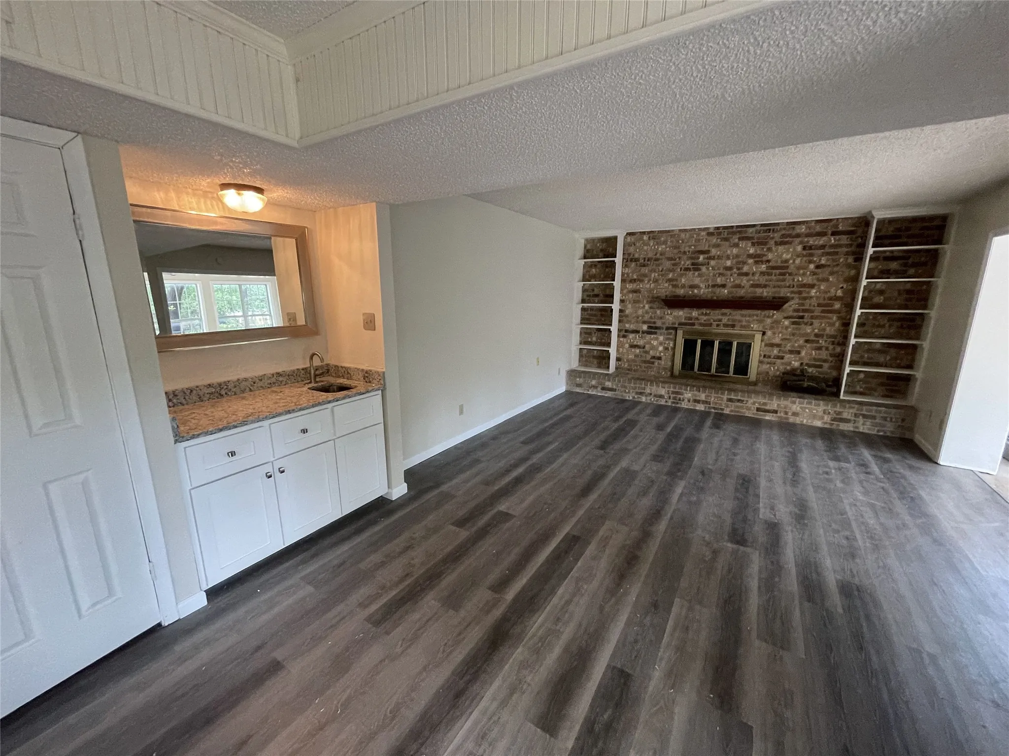 Wood-finish flooring throughout, featuring a brick-clad fireplace with built-in shelving, and a wet bar with white cabinetry and a granite-style countertop