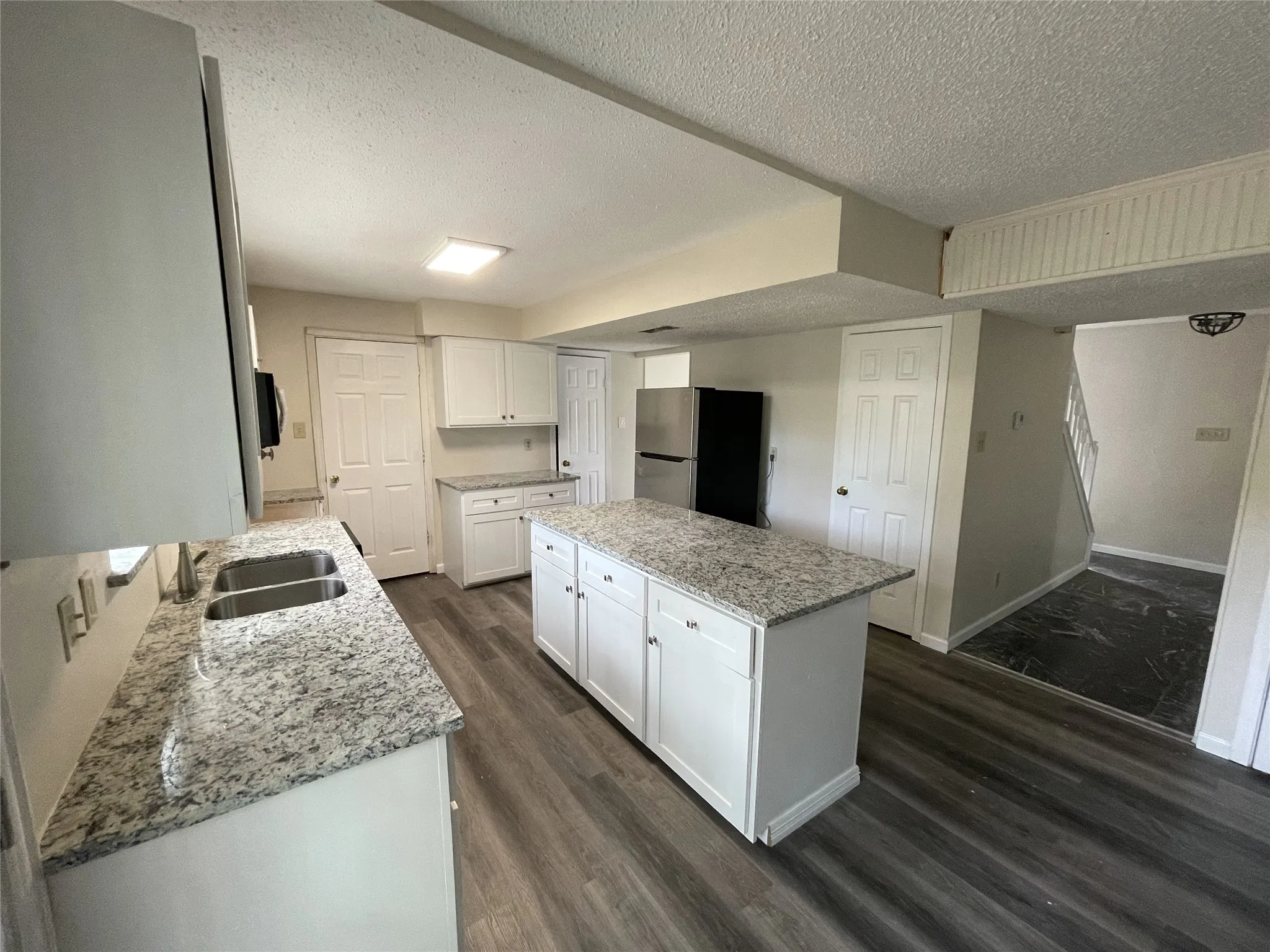 Kitchen featuring white cabinetry, light granite countertops, a double basin stainless steel sink, a central island, and wood-finish flooring