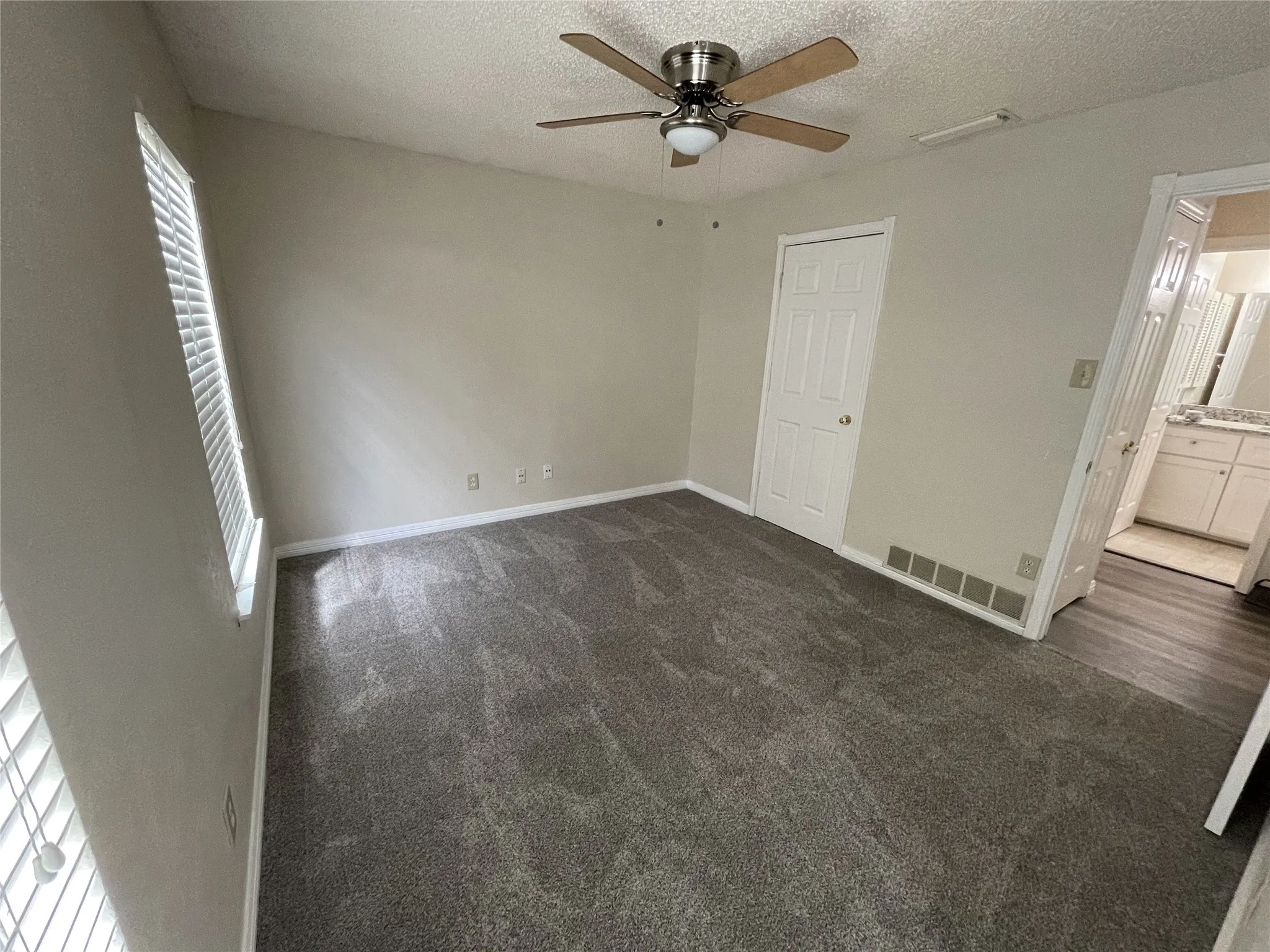Expansive room featuring plush grey carpeting, a ceiling fan with integrated lighting, and a window with blinds